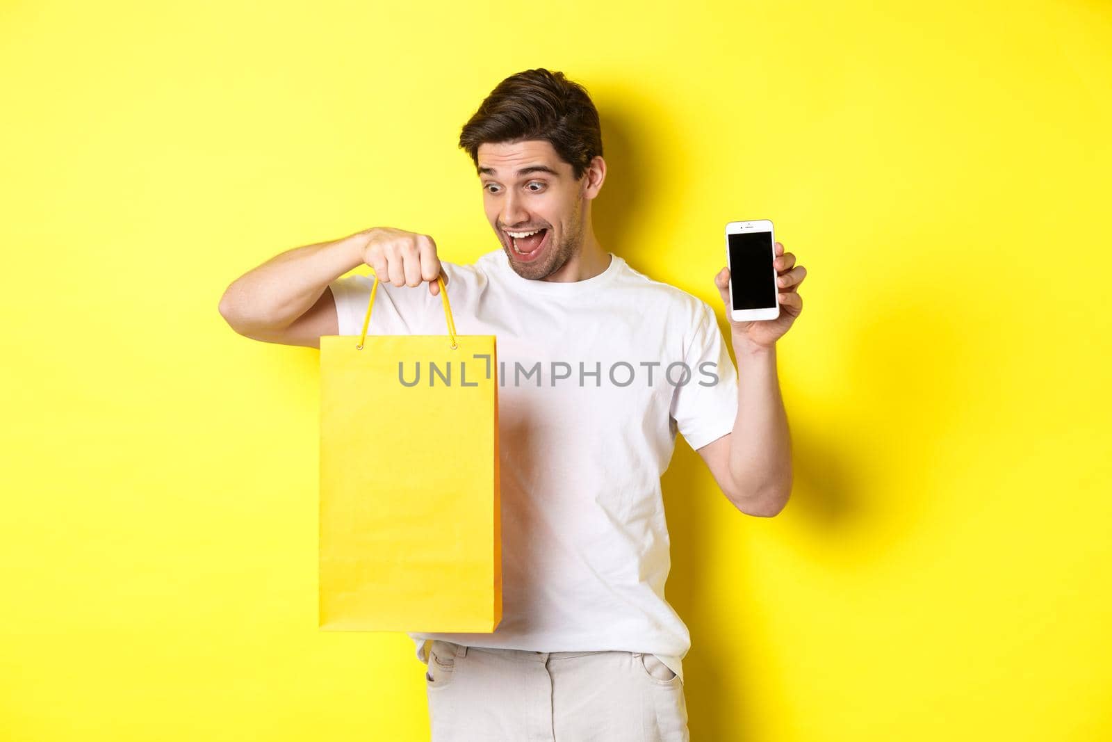 Happy man looking at shopping bag and showing mobile phone screen. Concept of online banking and money by Benzoix