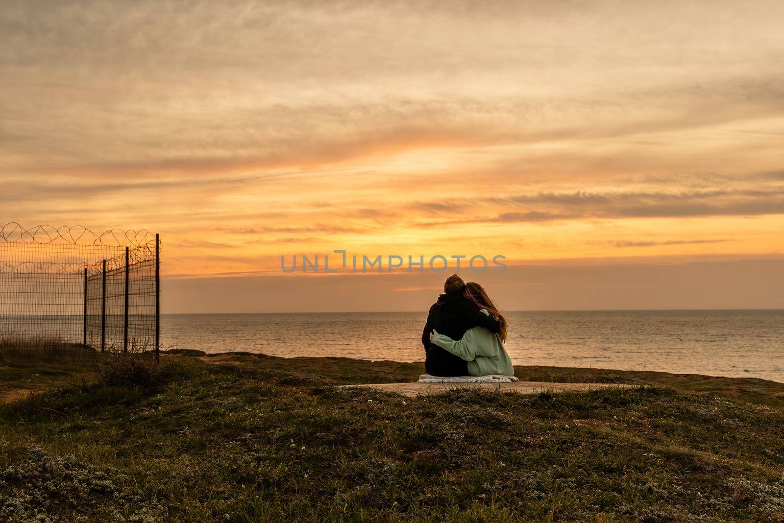Portraits of lovers, romantic couple of lovers hugging, kissing, touching, eye contact at sunset, sunrise against the background of the sea, sun, clouds in fiery red, orange colors.
