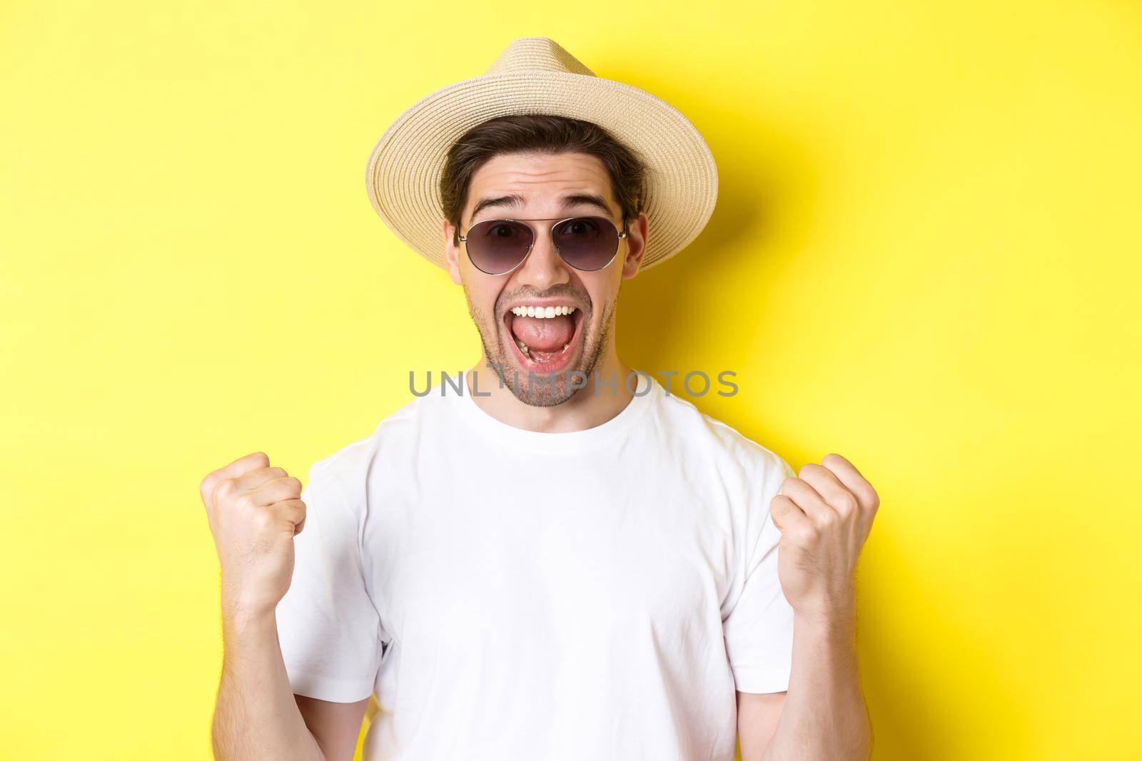 Concept of tourism and holidays. Lucky man tourist winning tickets, making fist pump and saying yes, wearing vacation clothes, standing over yellow background by Benzoix