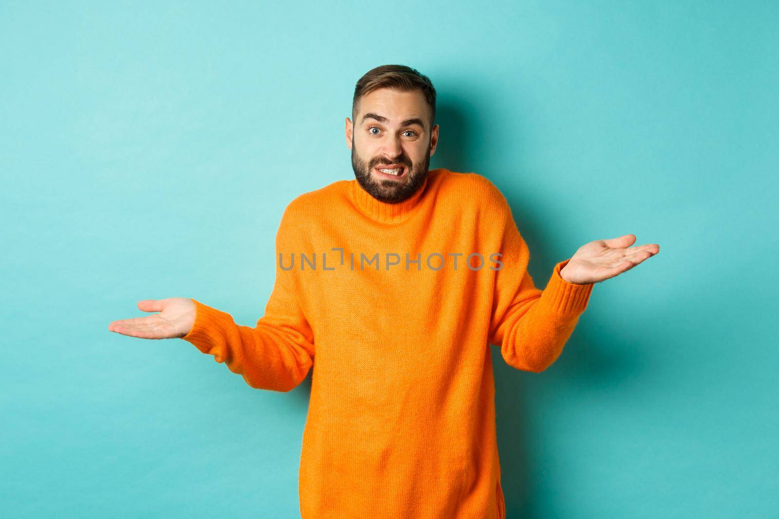 Confused caucasian man with beard, shrugging and looking clueless, standing indecisive against turquoise background by Benzoix
