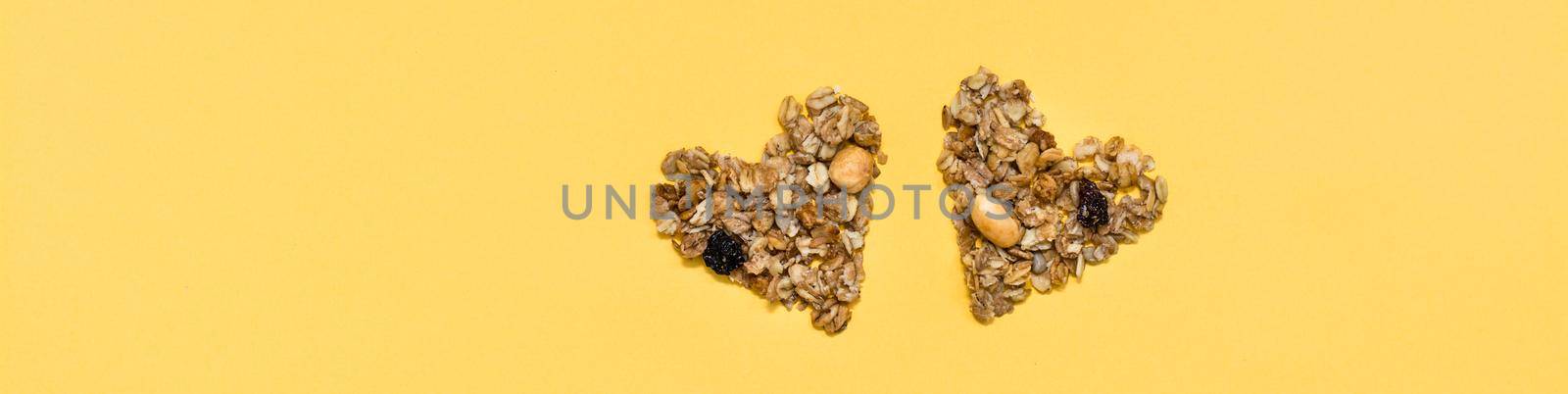 Love for healthy food. Granola made from oats, nuts and raisins in the form of two hearts on a yellow background. Top view. Web banner