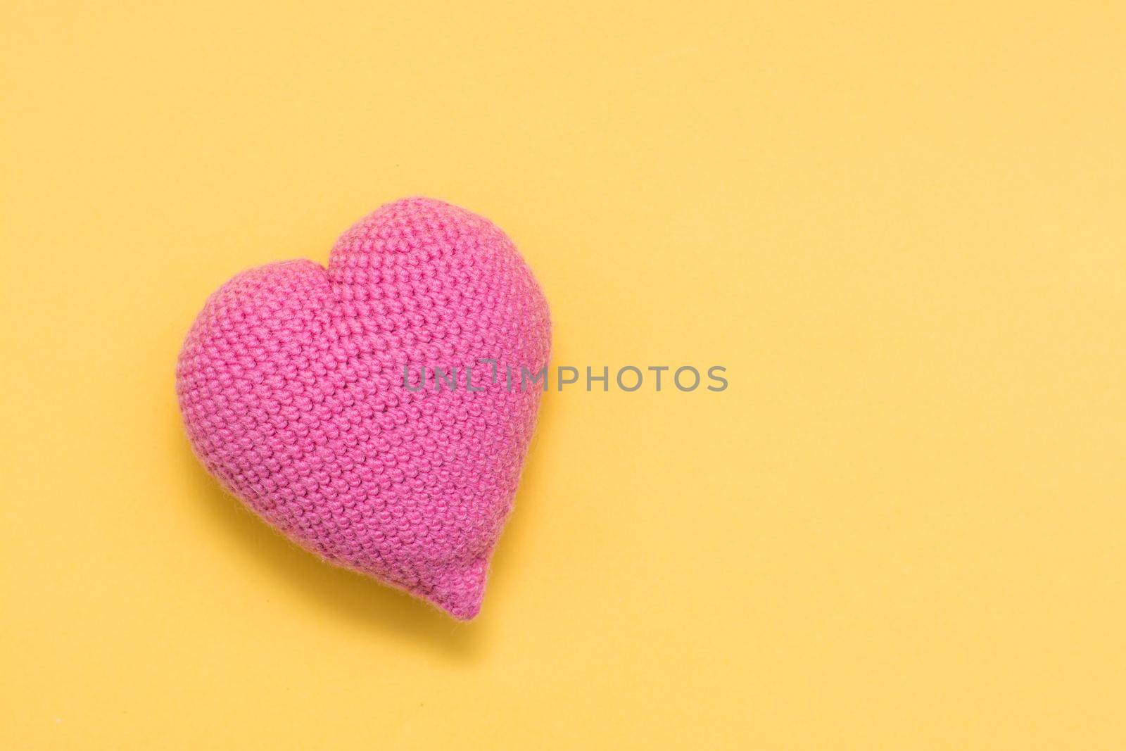 Handmade for Valentine's Day. Knitted big pink heart on a yellow background. Copy space by Aleruana