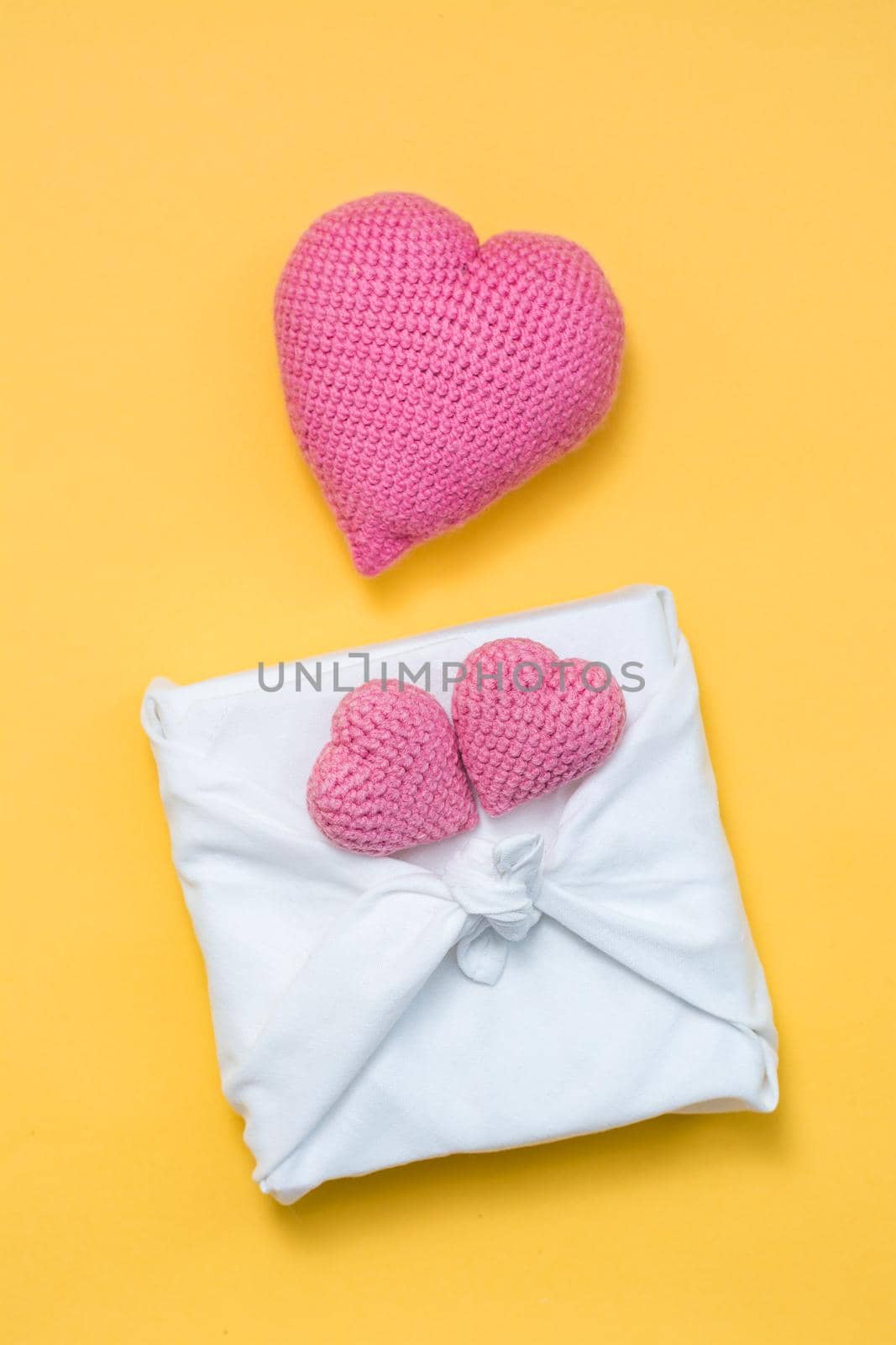 Zero waste valentine's day. Eco friendly gift furoshiki and knitted hearts on yellow background. Vertical view