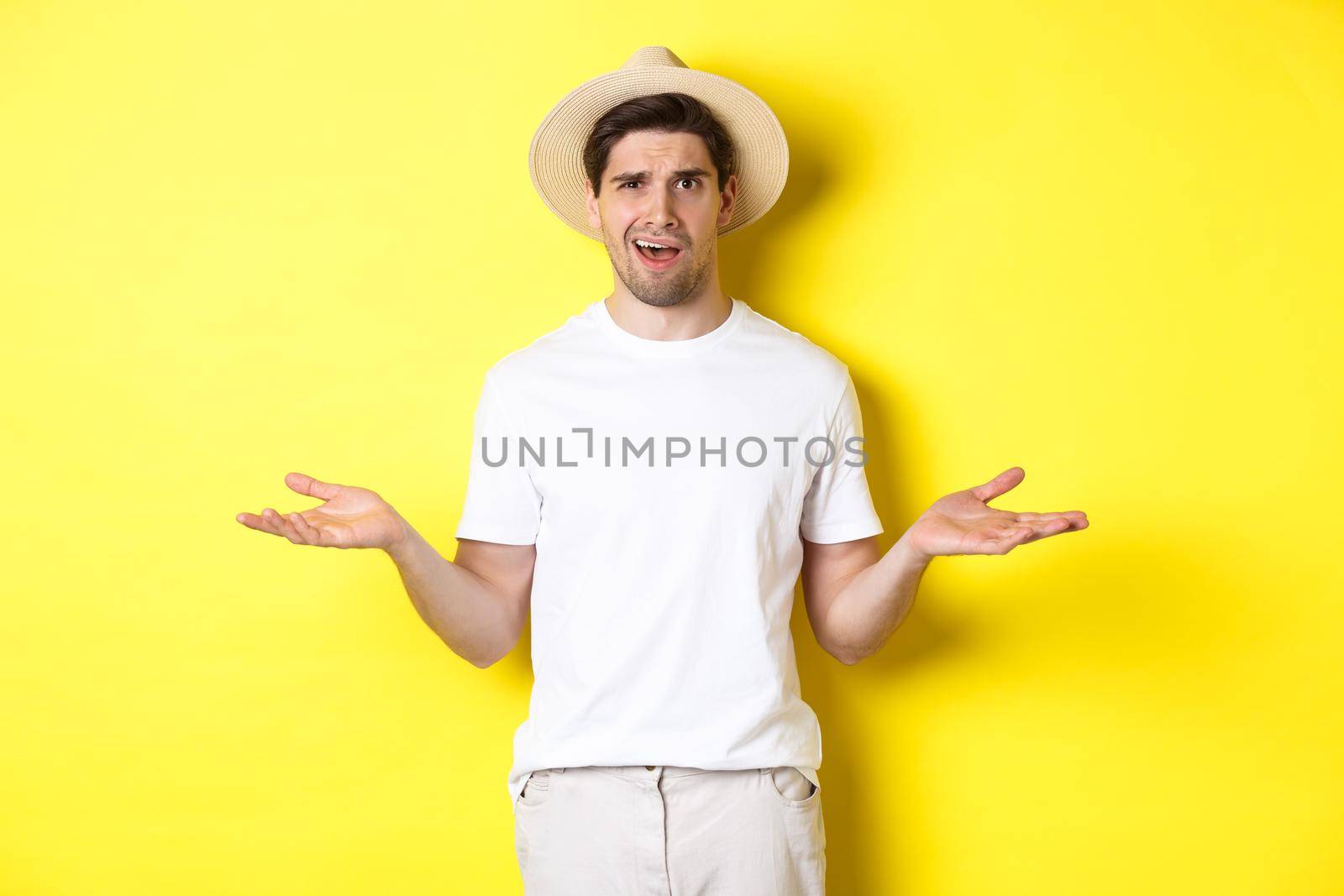 Concept of tourism and summer. Confused guy traveller shrugging, cant understand something, standing against yellow background by Benzoix