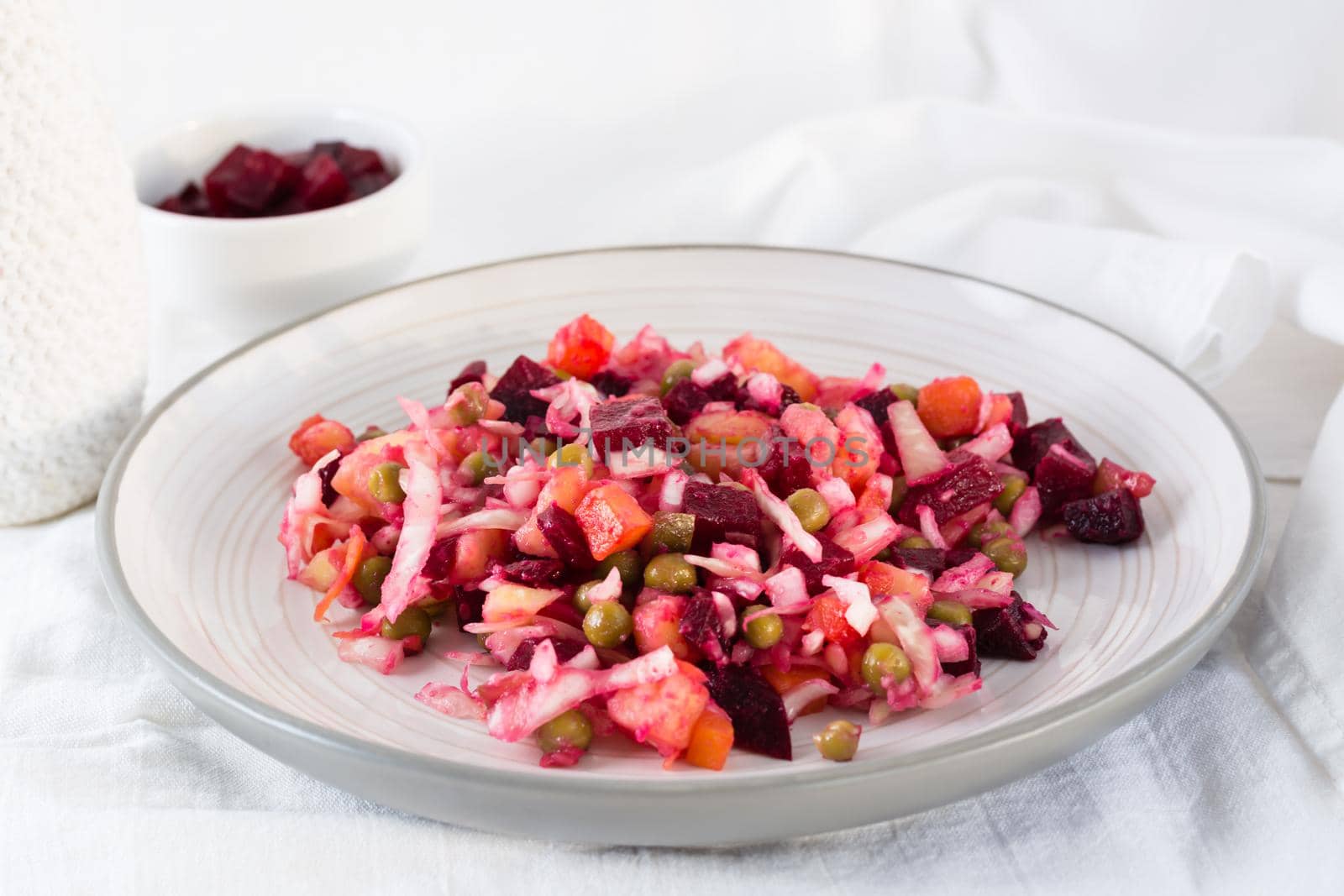 Russian traditional salad with vegetables - vinaigrette on a plate and a bowl of beets on a table on a cloth. Close-up by Aleruana
