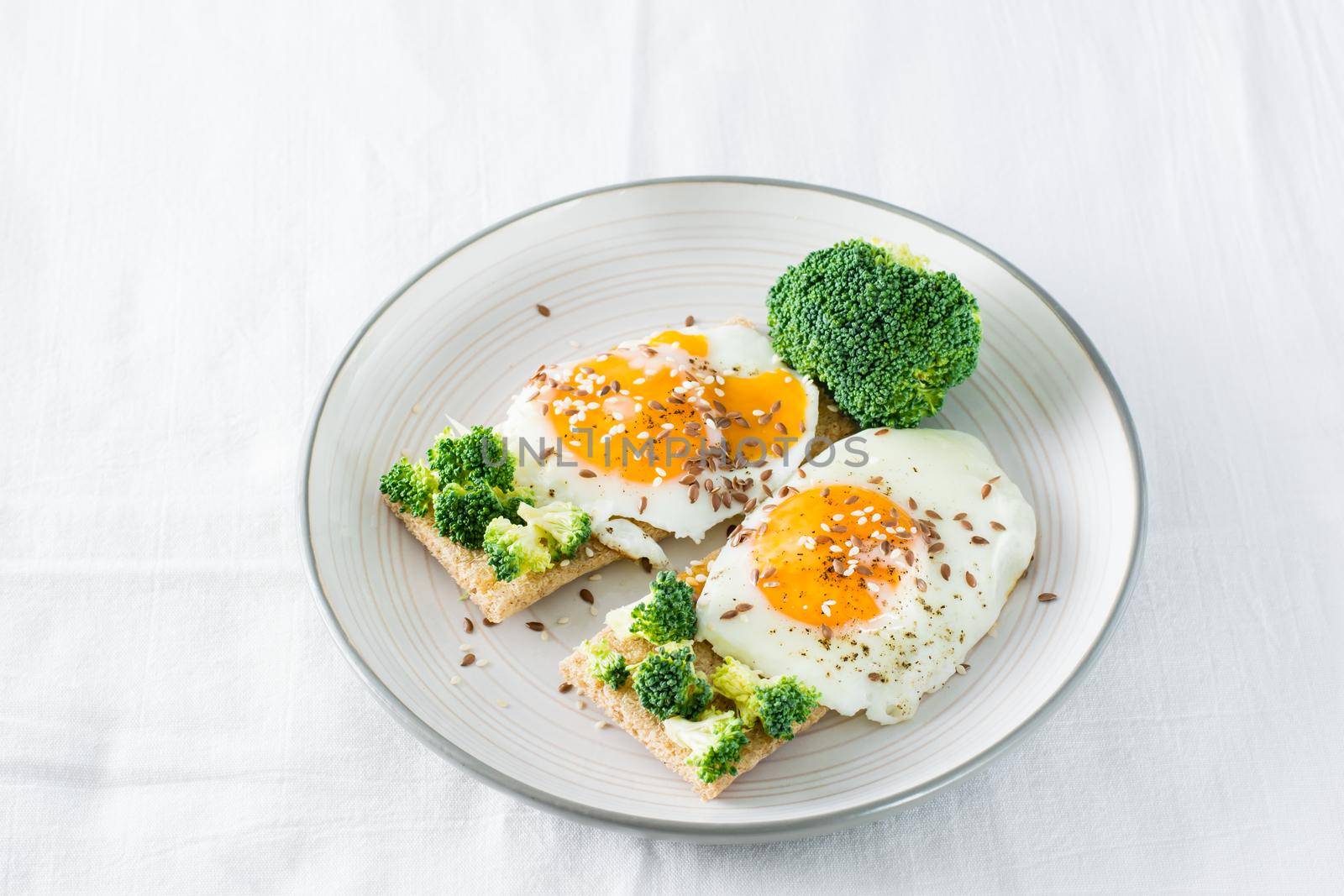 Bruschetta with scrambled eggs and broccoli on a grain crispbread on a plate on the table by Aleruana