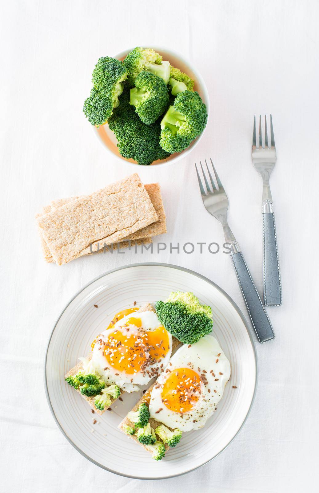 Bruschetta with scrambled eggs and broccoli on a grain crispbread with sesame seeds and flaxseed on a plate on the table. Top view. Vertical view