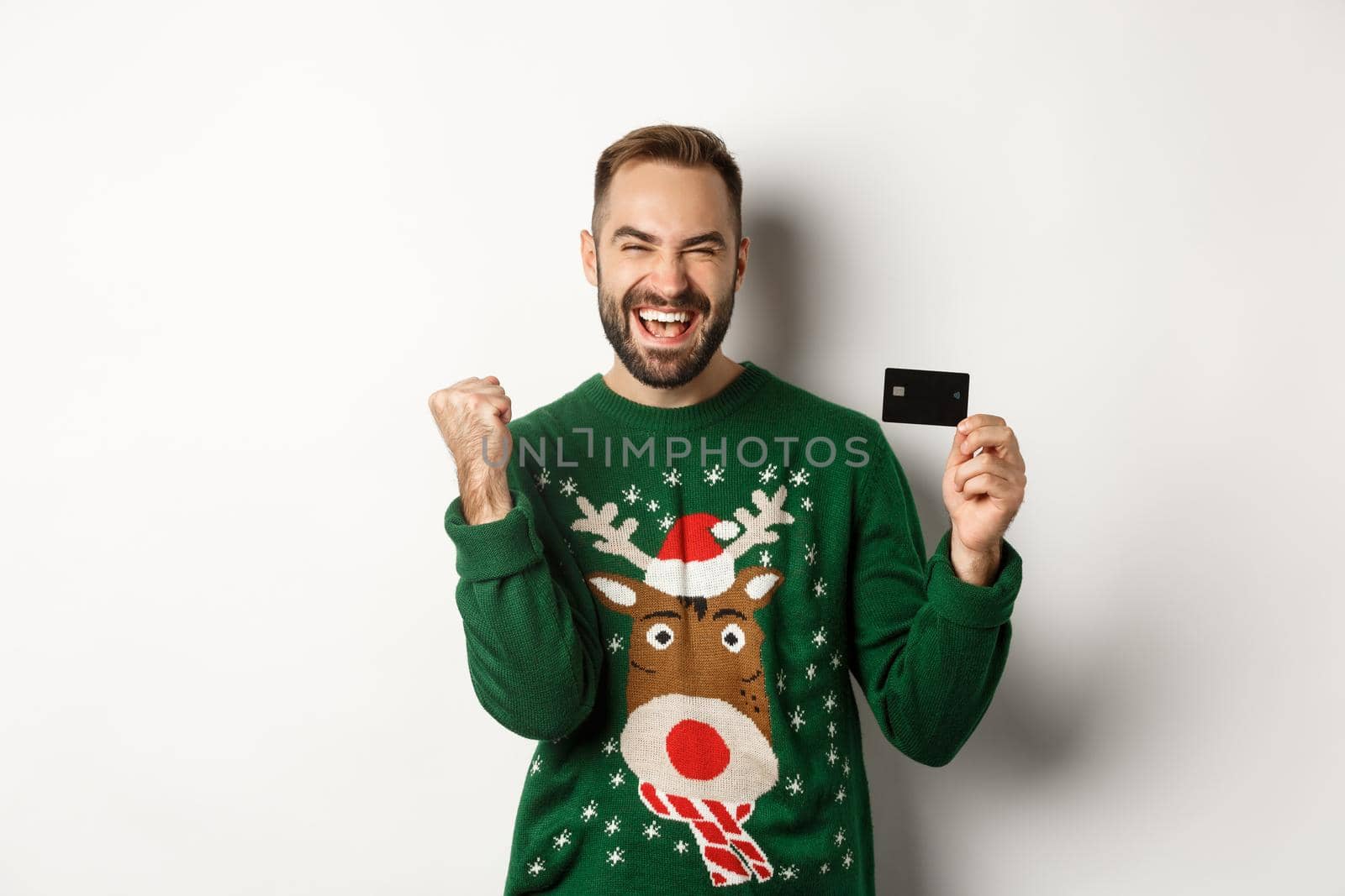 Christmas holidays and shopping concept. Excited man showing credit card and looking happy, standing over white background.