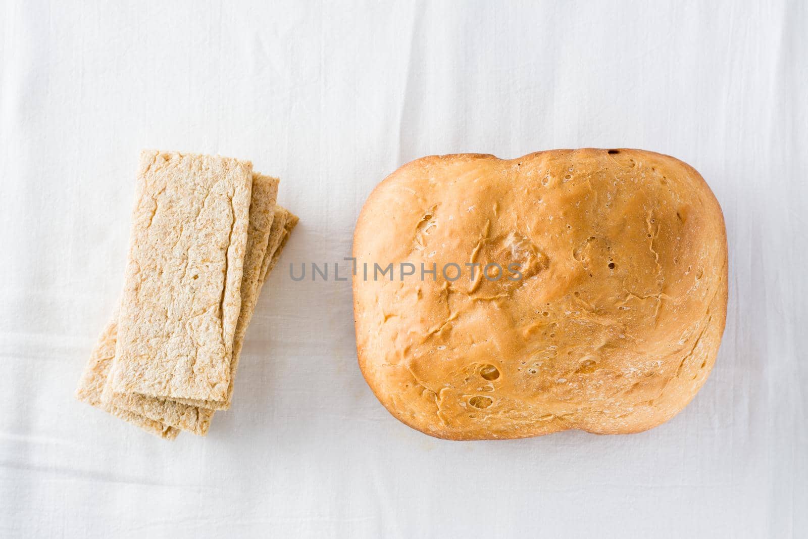 Concept of choice between fresh loaf of wheat homemade bread and cereal crispbread on white cloth. Top view