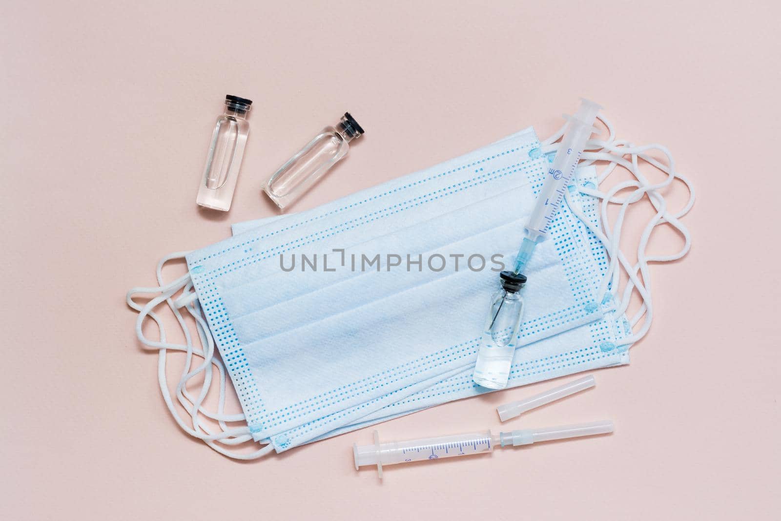 Vaccination and Immunization. Syringe needle inserted into a glass vial with vaccine on a face protective mask and other vials and syringes. Top view by Aleruana