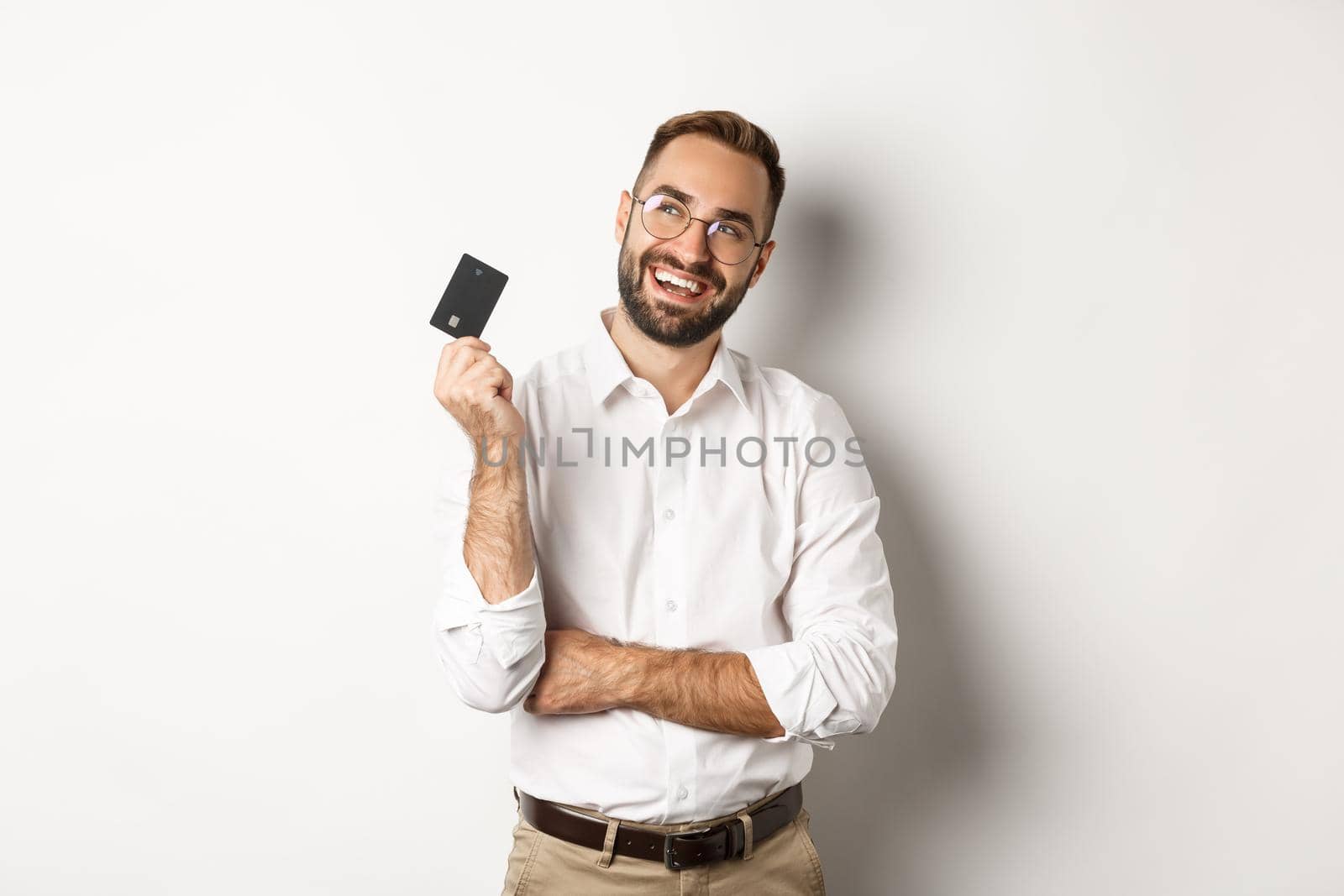 Image of handsome man thinking about shopping and holding credit card, looking at upper left corner thoughtful, white background by Benzoix