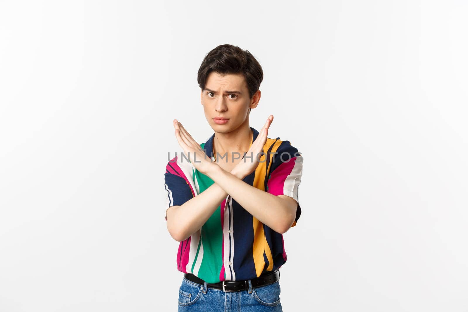 Disappointed young queer man telling no, showing stop gesture and forbid something bad, standing over white background by Benzoix