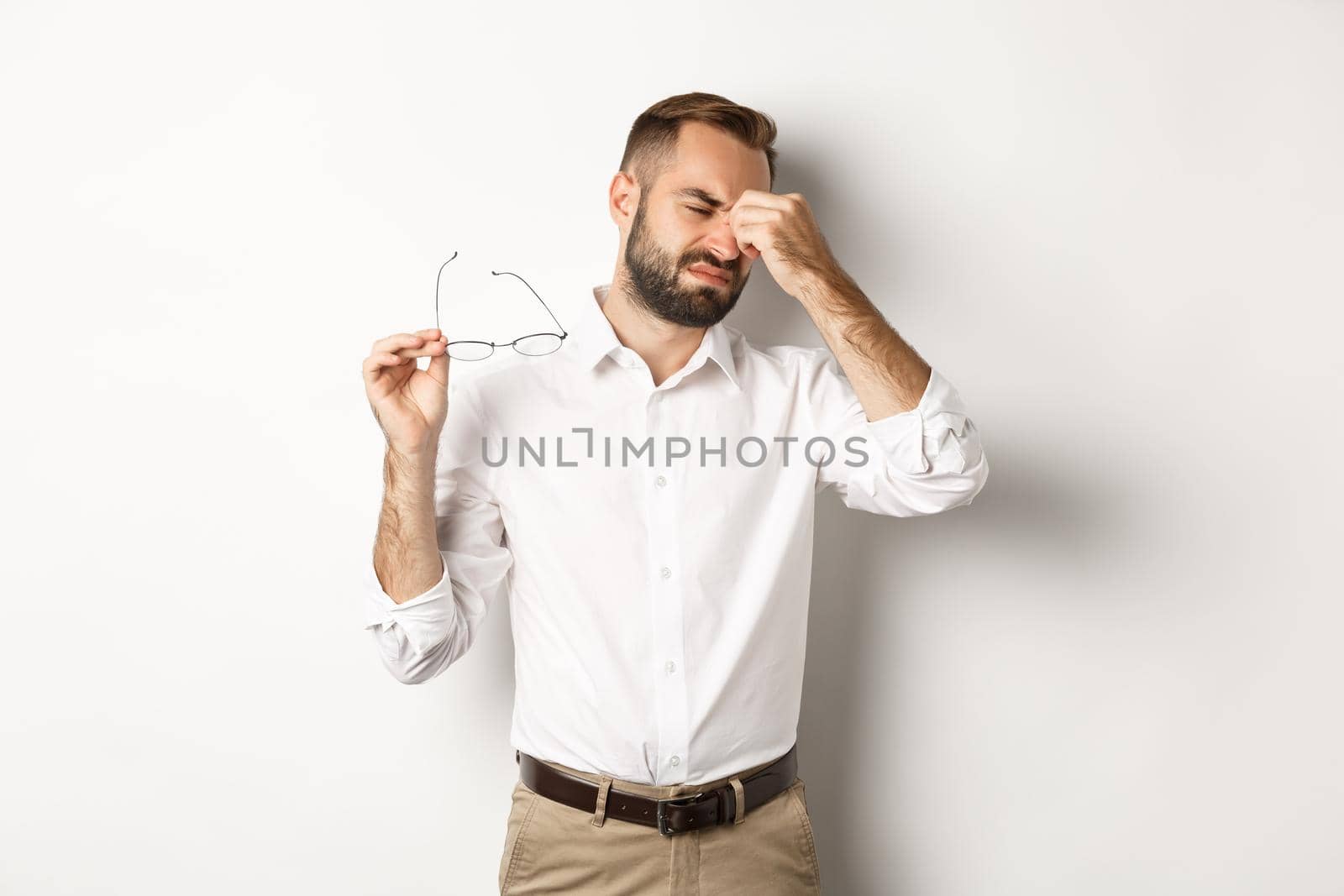 Tired businessman take-off glasses and rubbing eyes, standing exhausted against white background.