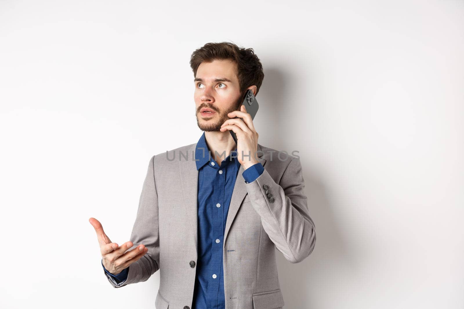 Businessman making phone call, talking on smartphone and looking busy, wearing suit, white background.