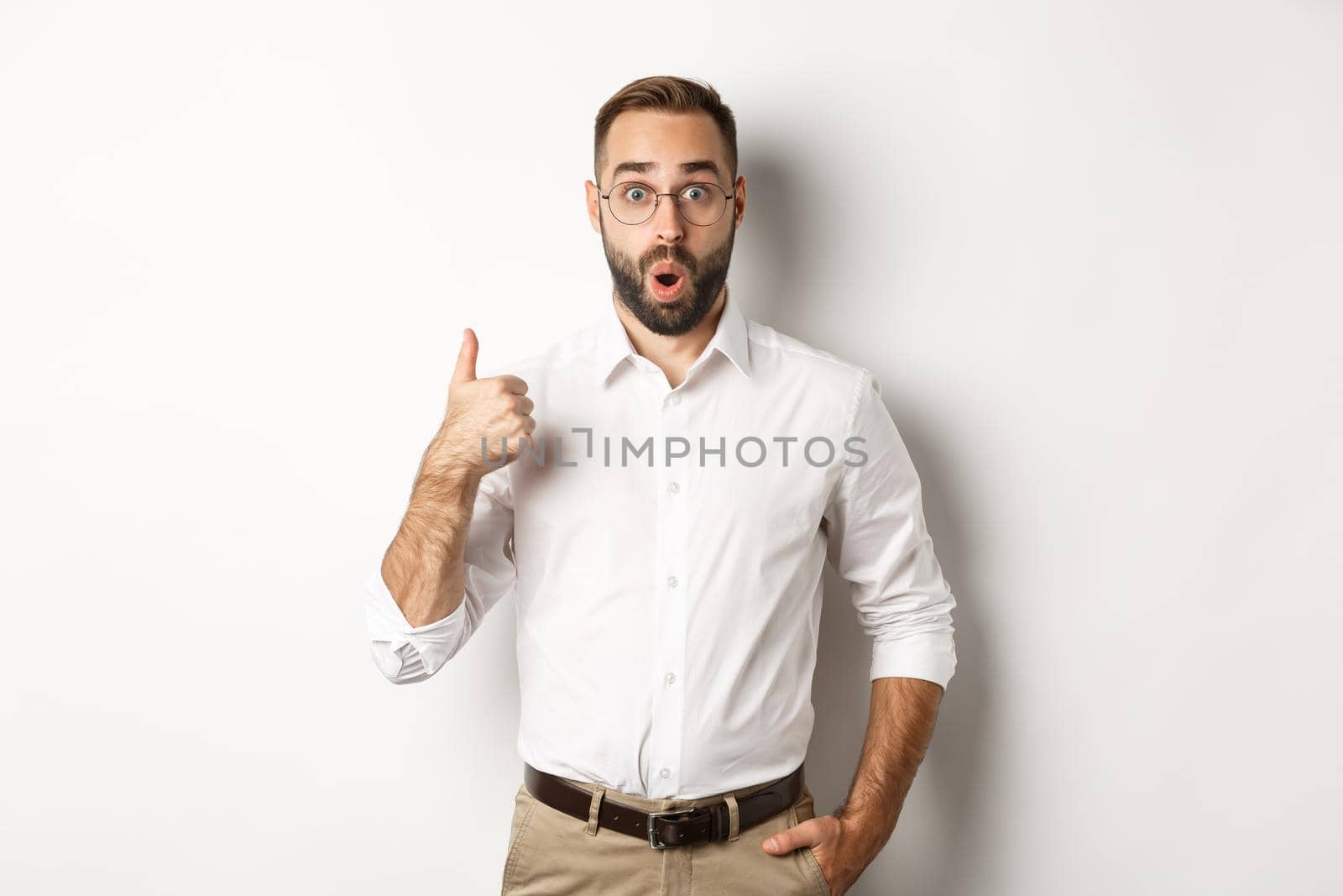 Impressed young male entrepreneur showing thumbs-up, praise something good, like and agree, white background.