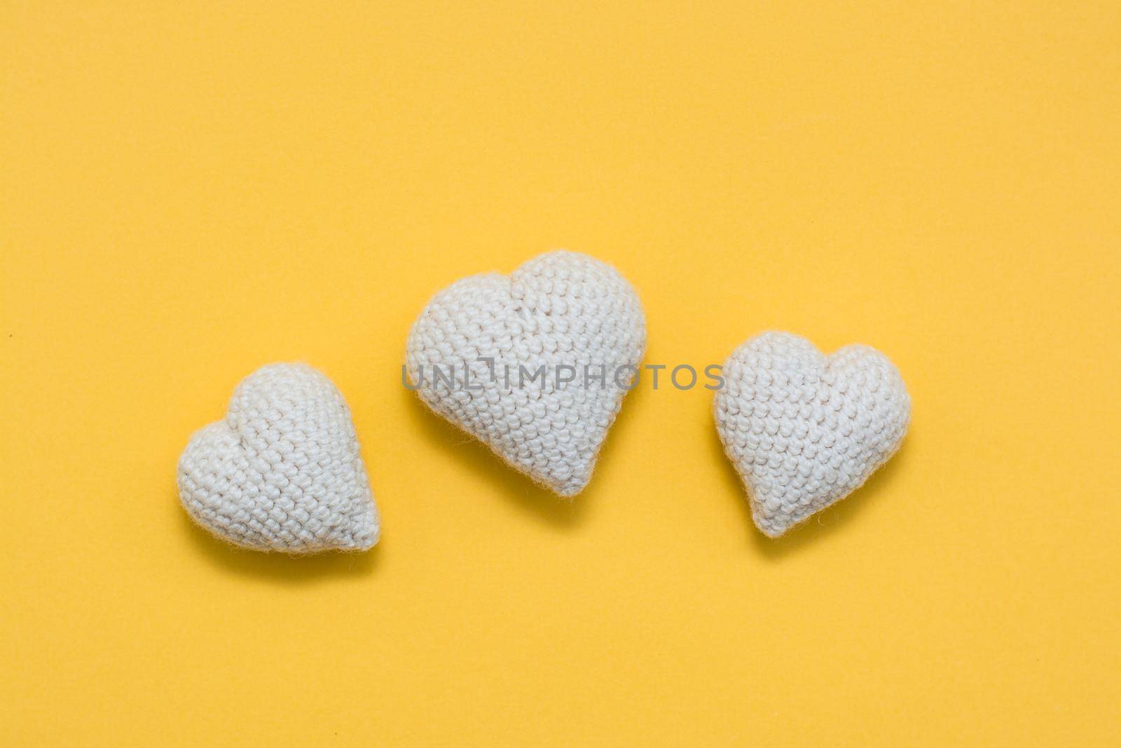 Handmade for Valentine's Day. Knitted white hearts on a yellow background