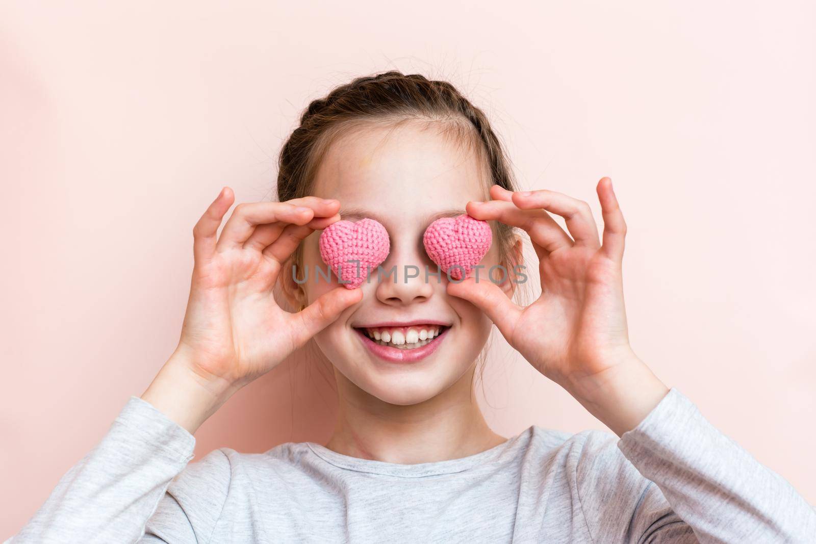 Cheerful smiling girl holding knitted hearts in front of her eyes