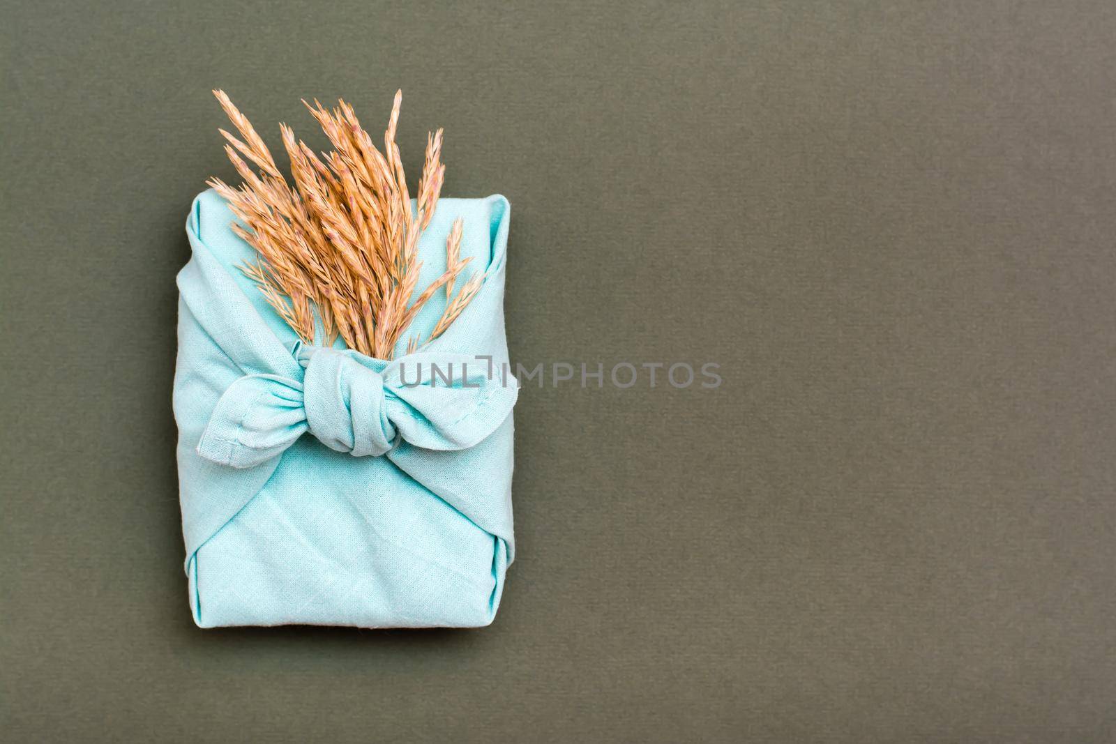 Eco friendly furoshiki gift with ears of dry grass on green background