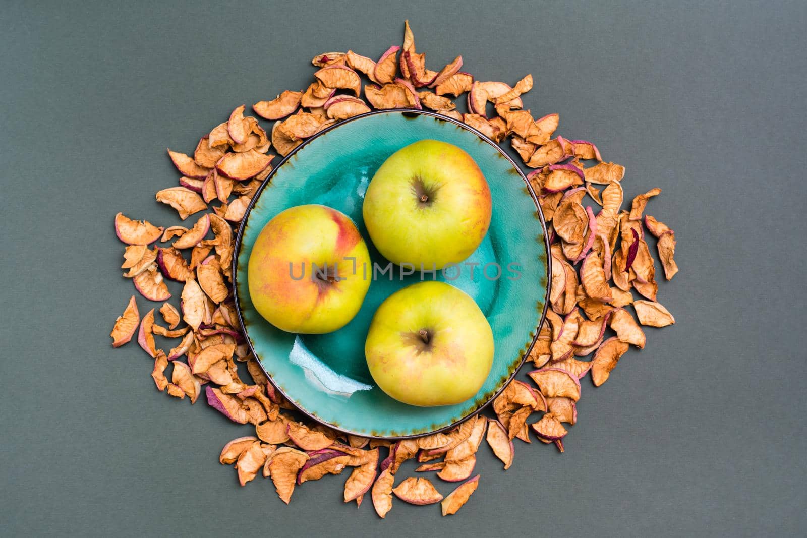 Fresh apples on a plate and pieces of dry apples around on a green background. Top view by Aleruana