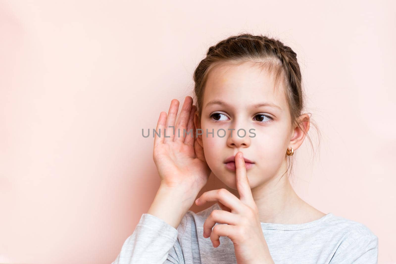 Sad girl holding her finger in front of her lips and hand near her ear listening. Call for silence