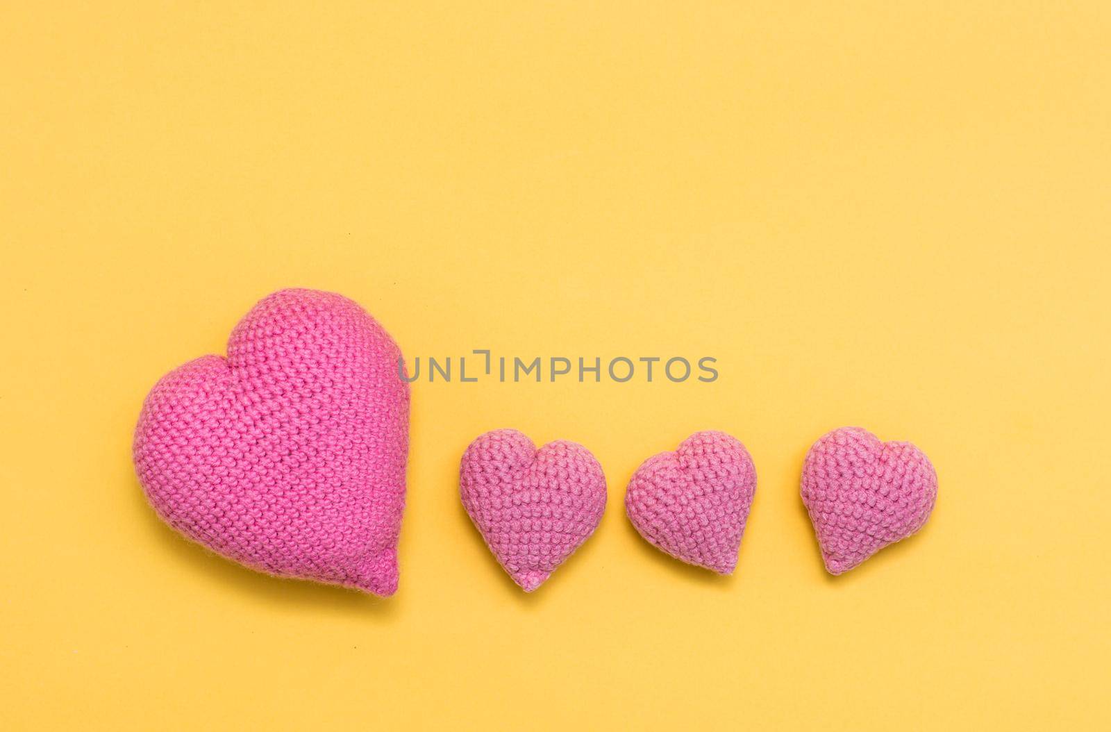 Handmade for Valentine's Day. Knitted large and small pink hearts on a yellow background. Copy space