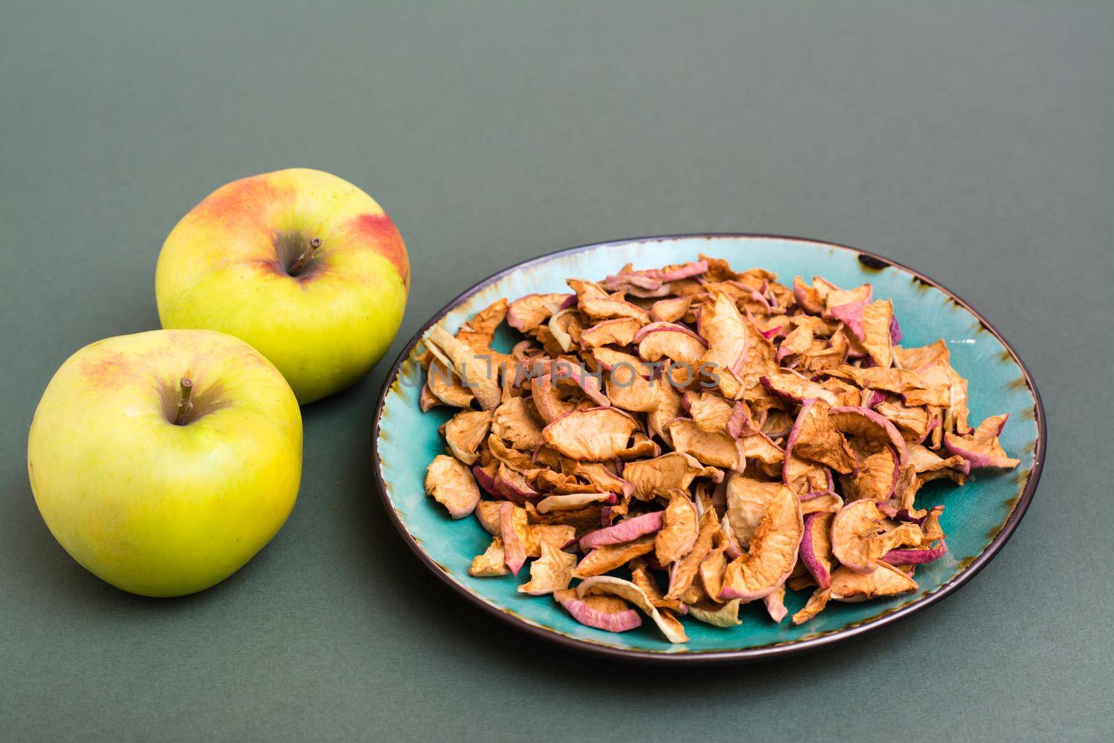 Slices of dry apples on a plate and fresh apples on a green background. Healthy eating