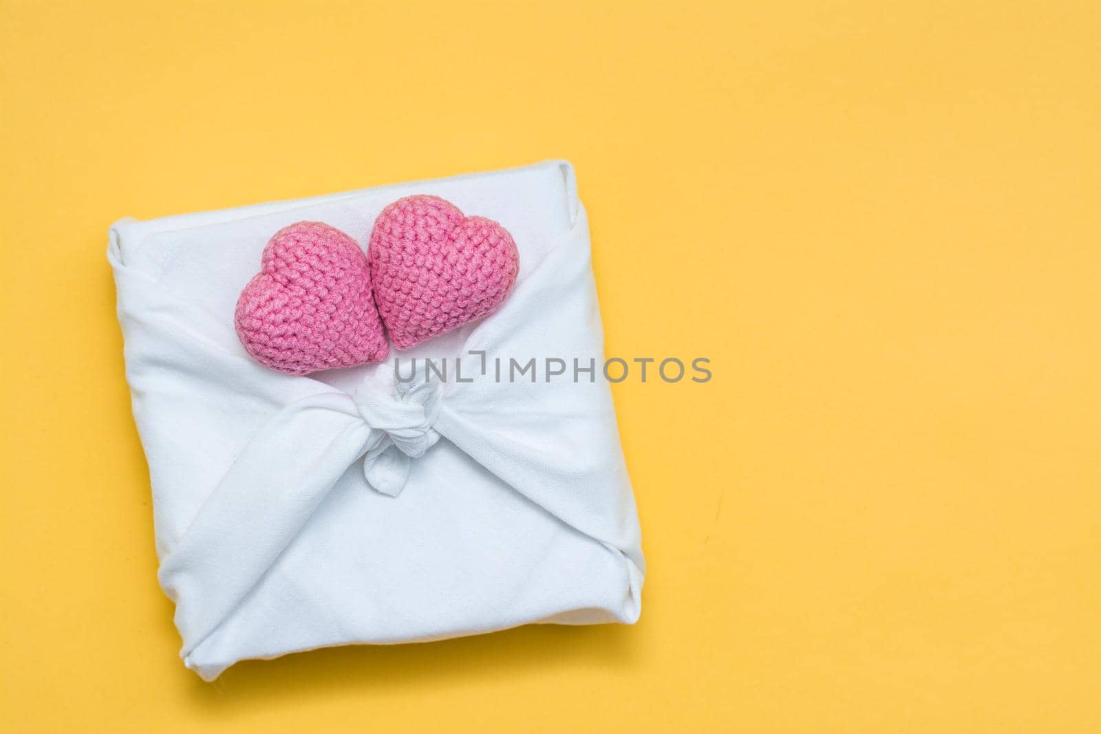 Zero waste valentine's day. Eco friendly gift furoshiki and knitted hearts on yellow background. Copy space. Top view by Aleruana