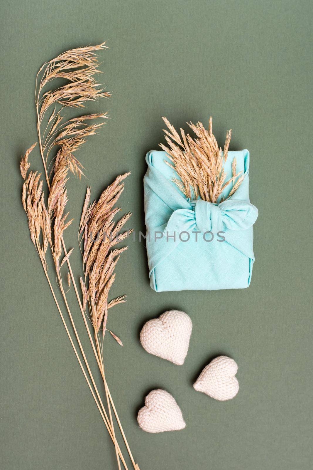 Eco friendly valentine's day gift furoshiki, knitted hearts and ears of dry grass on green background. Vertical view