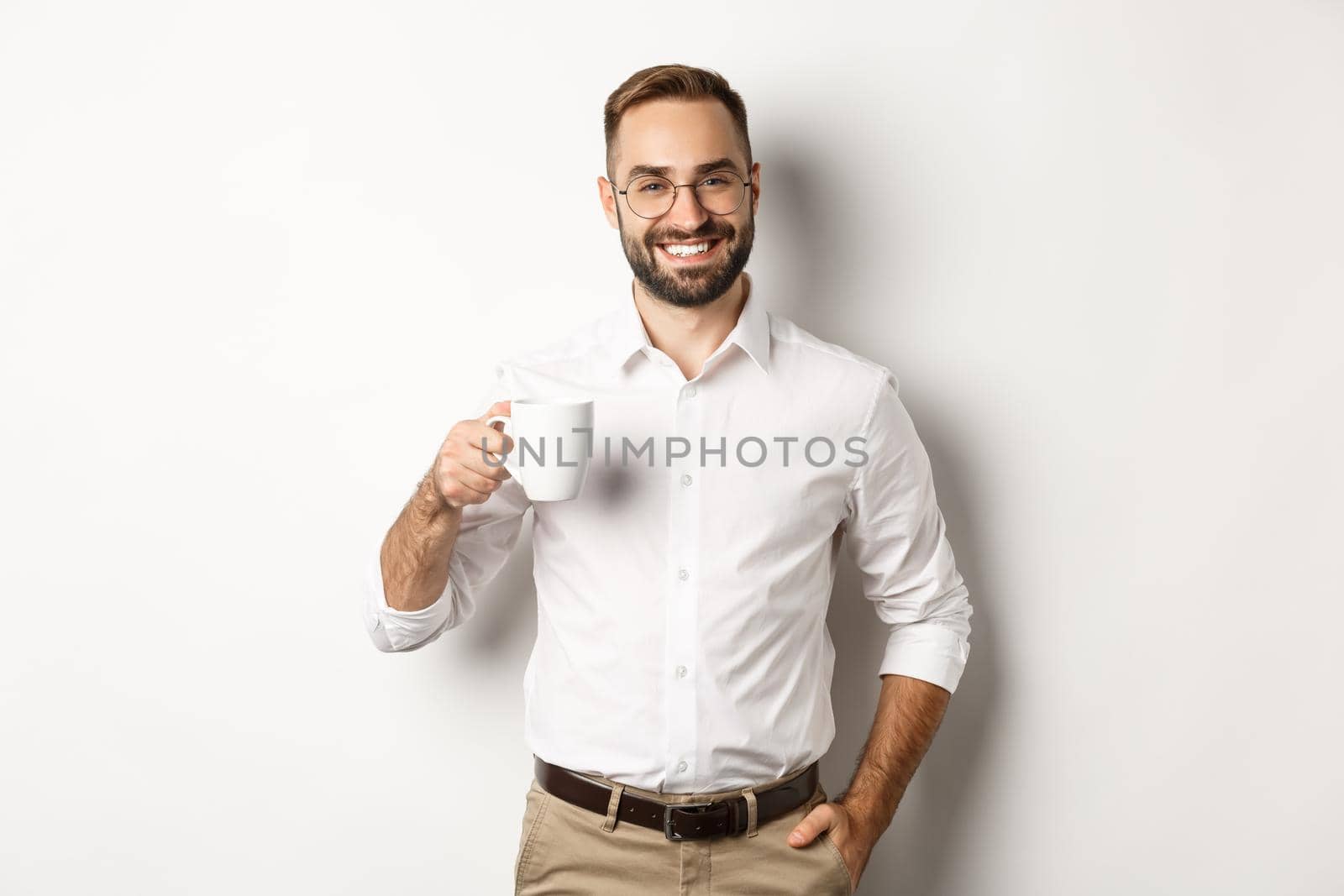 Handsome businessman drinking coffee and smiling, standing against white background.