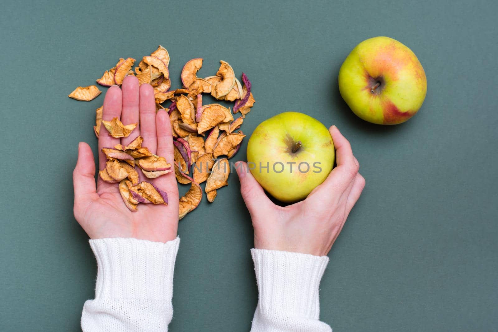 Female hands hold a handful of pieces of dry apples and fresh apples on a green background by Aleruana