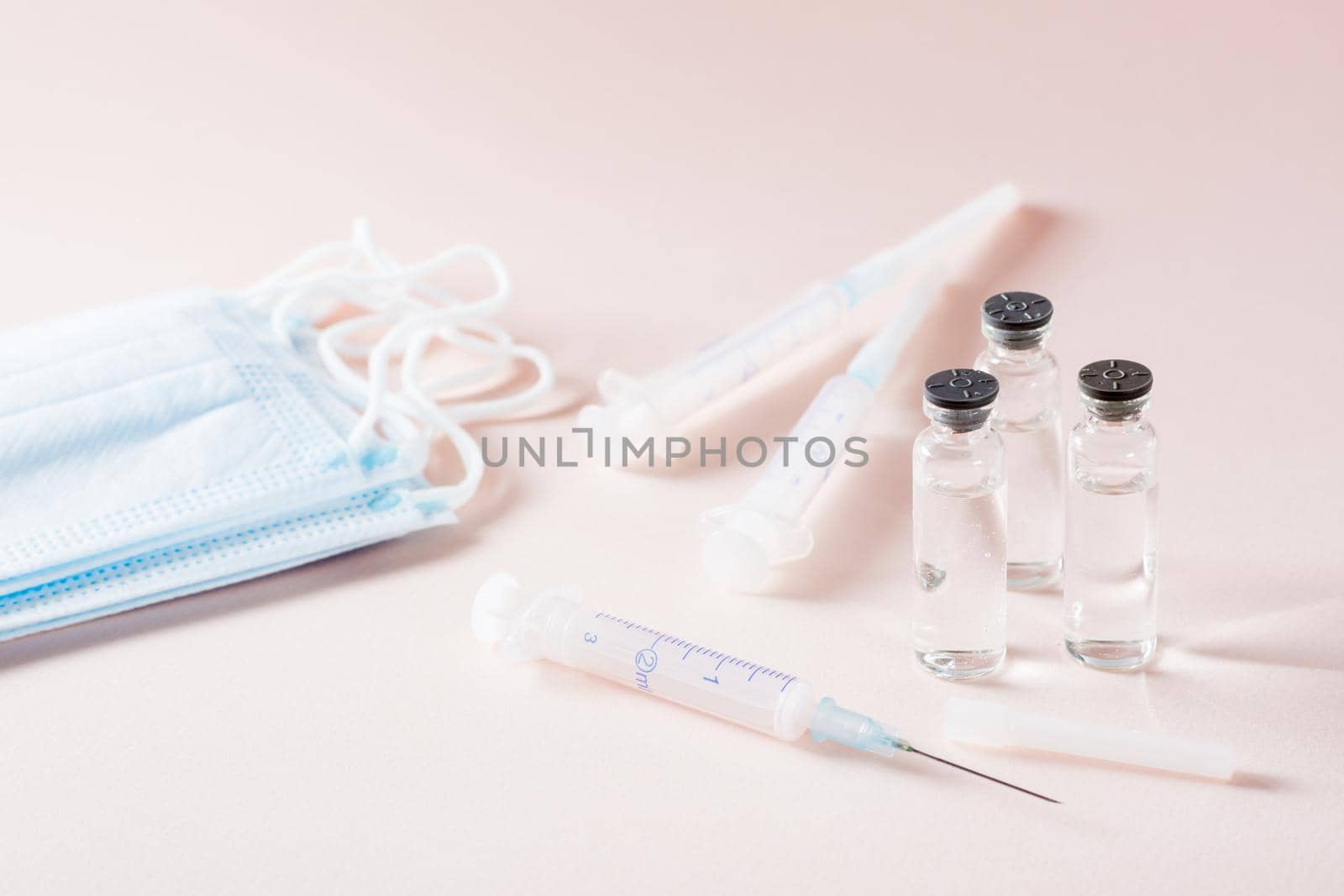 Vaccination and Immunization. Opened syringe in front of glass vials with vaccine, protective masks and clean syringes by Aleruana