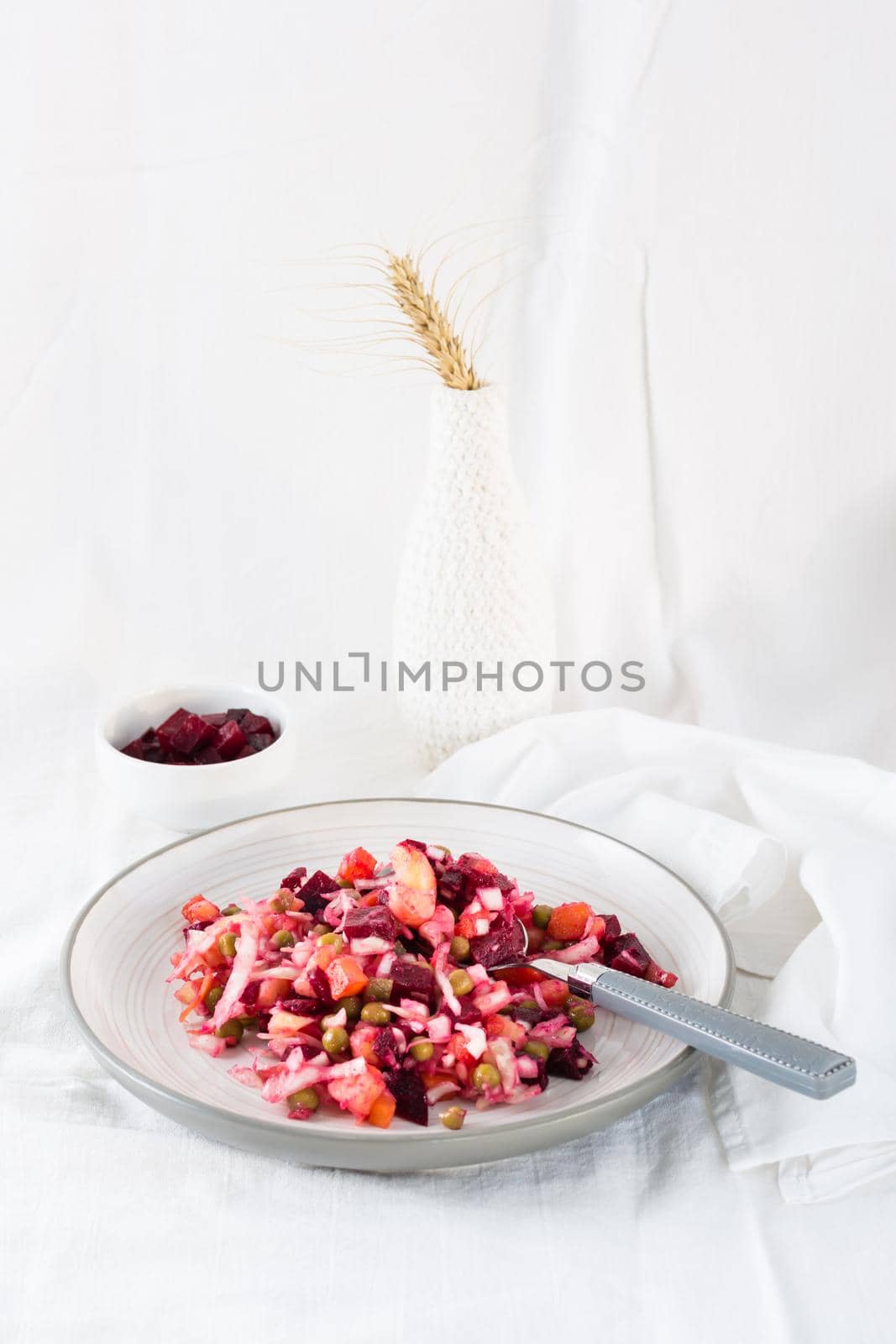 Russian traditional salad with vegetables - vinaigrette and spoon  on a plate and a bowl of beets on a table on a cloth. Vertical view by Aleruana