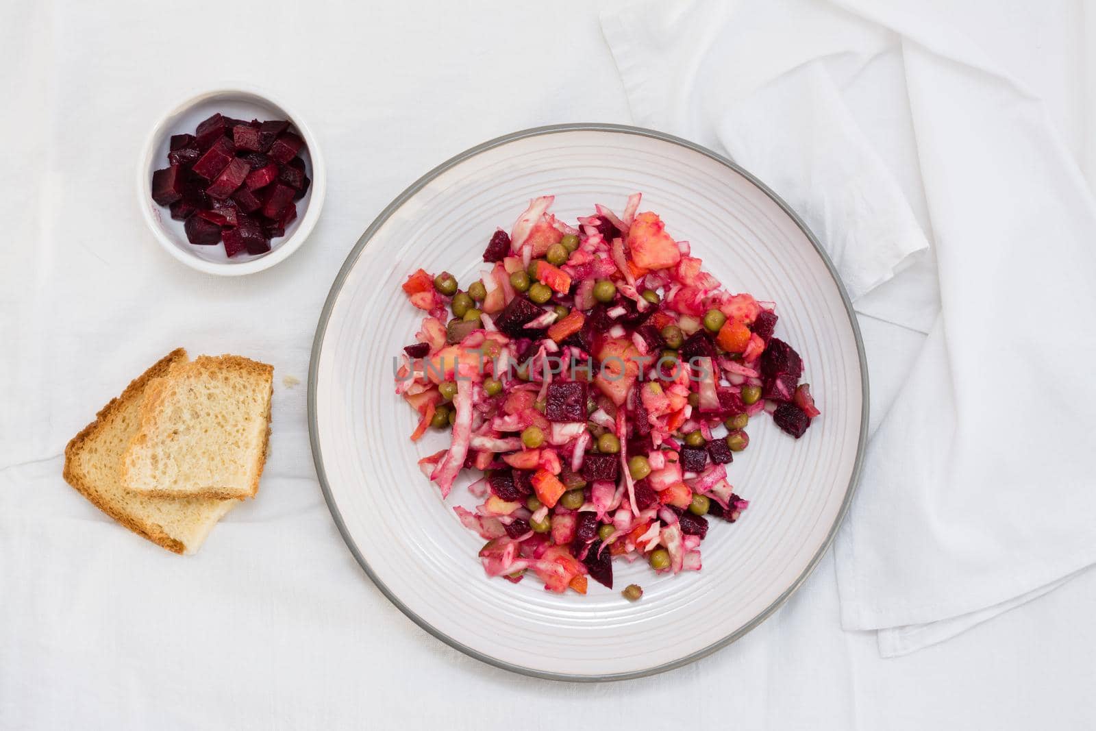 Russian traditional salad with vegetables - vinaigrette on a plate, bread and a bowl of beets on a table on a cloth. Top view by Aleruana