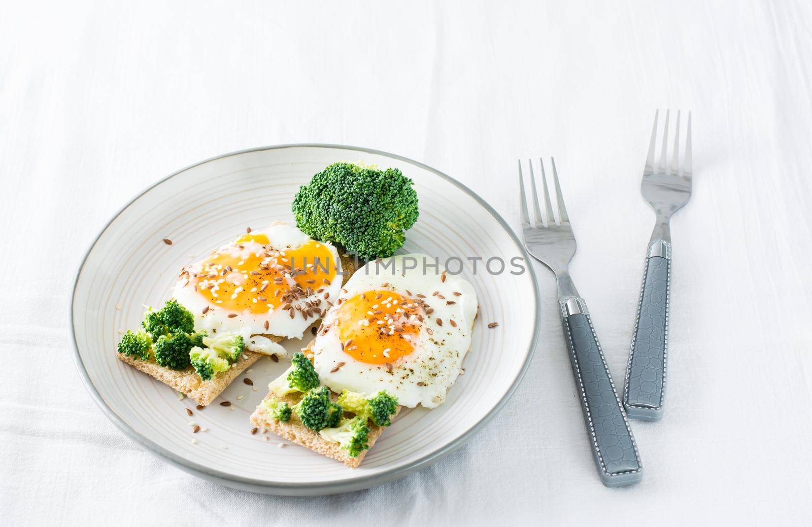 Bruschetta with scrambled eggs and broccoli on a grain crispbread with sesame seeds and flaxseed on a plate on the table by Aleruana
