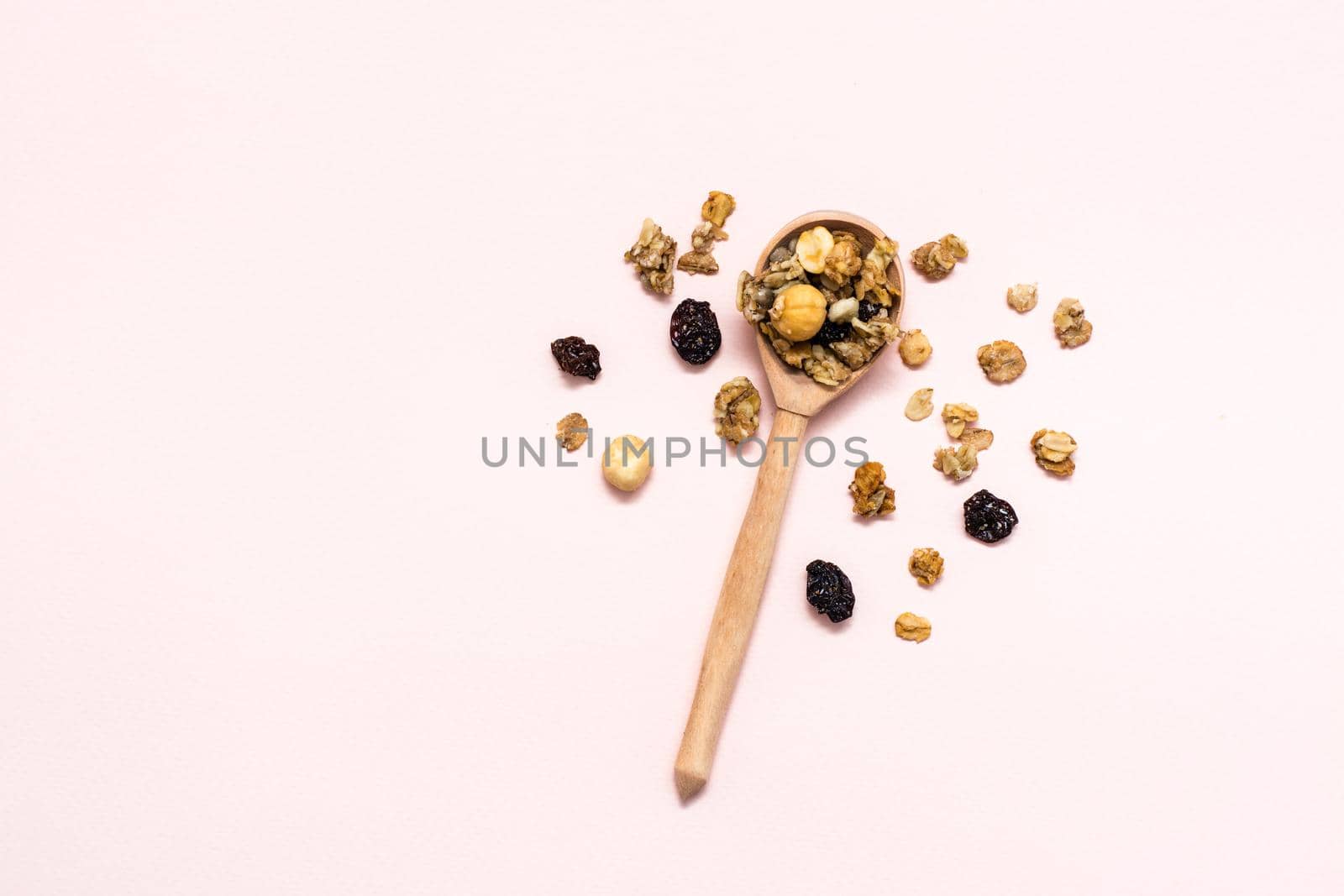 Healthy eating. Baked granola of oats, nuts and raisins in a wooden spoon on a pink background. Top view