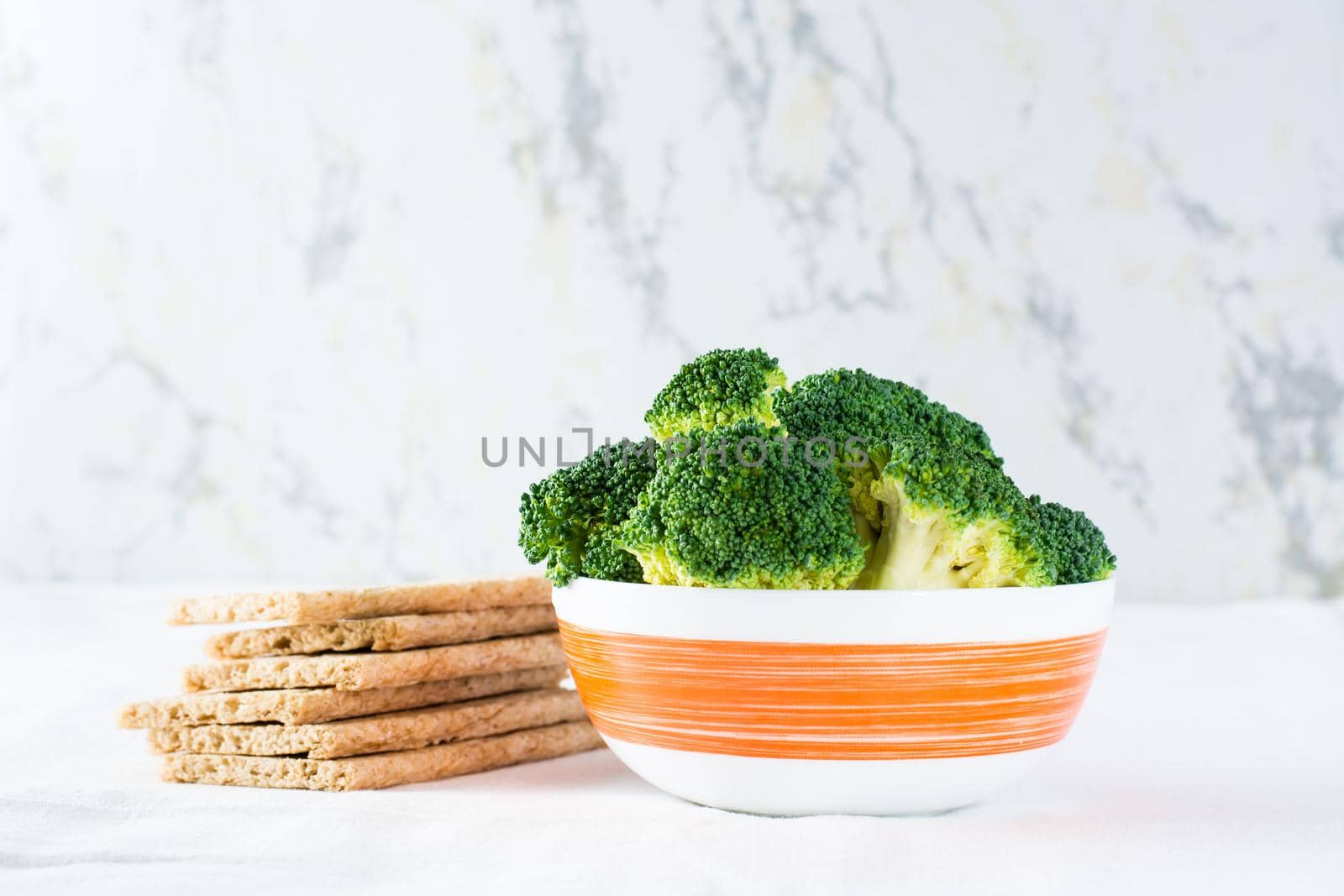 Fresh broccoli in a bowl and grain crispy bread on a table on a cloth. Copy space