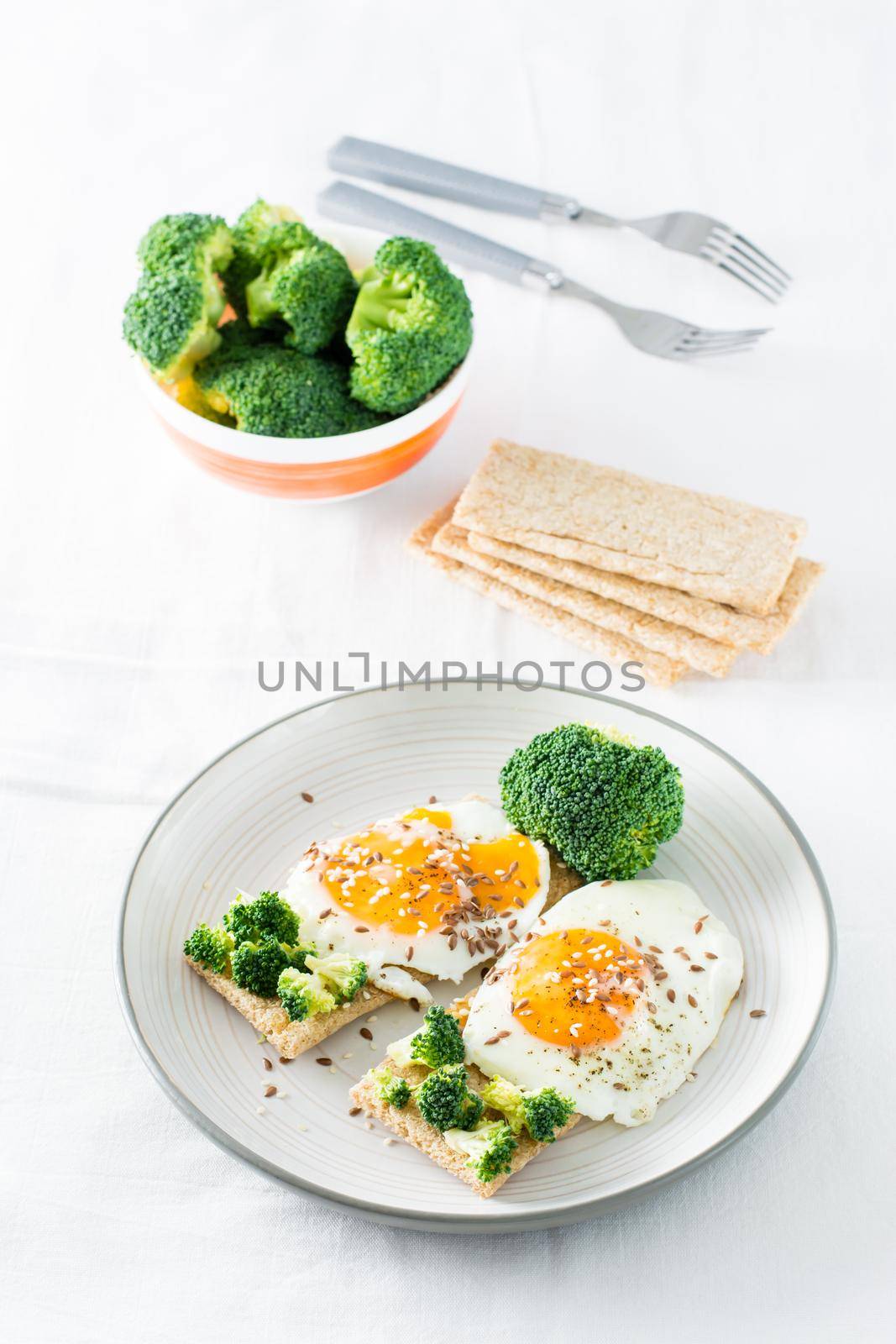 Bruschetta with scrambled eggs and broccoli on a grain crispbread with sesame seeds and flaxseed on a plate on the table.  Vertical view