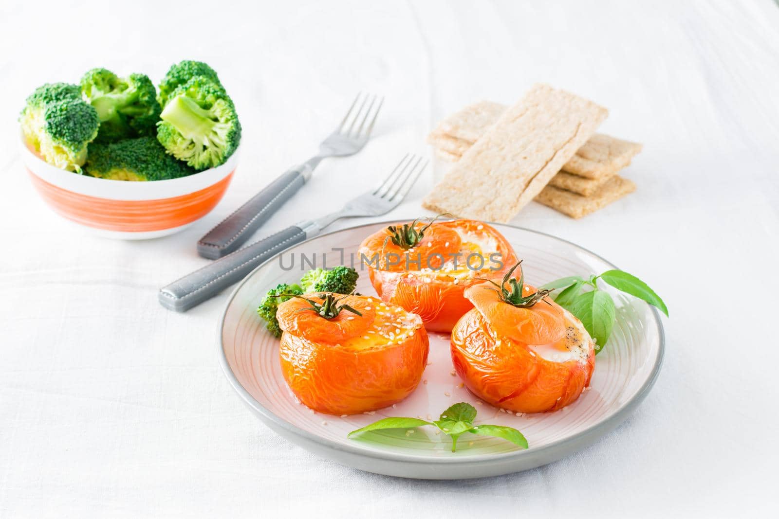 Baked tomatoes with egg, broccoli and basil leaves on a plate and a bowl of fresh broccoli. Diet lunch
