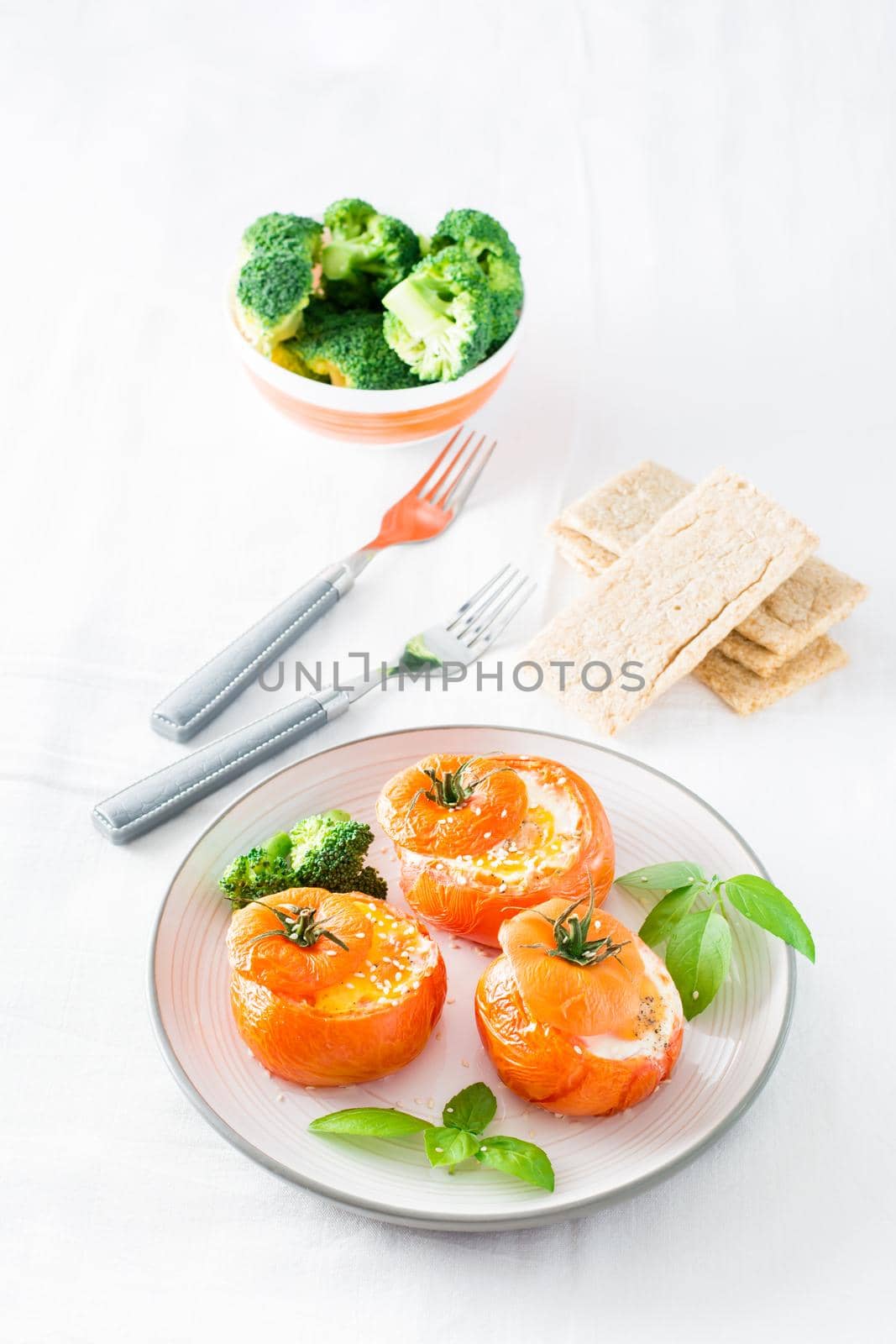 Baked tomatoes with egg, broccoli and basil leaves on a plate. Diet lunch. Vertical view