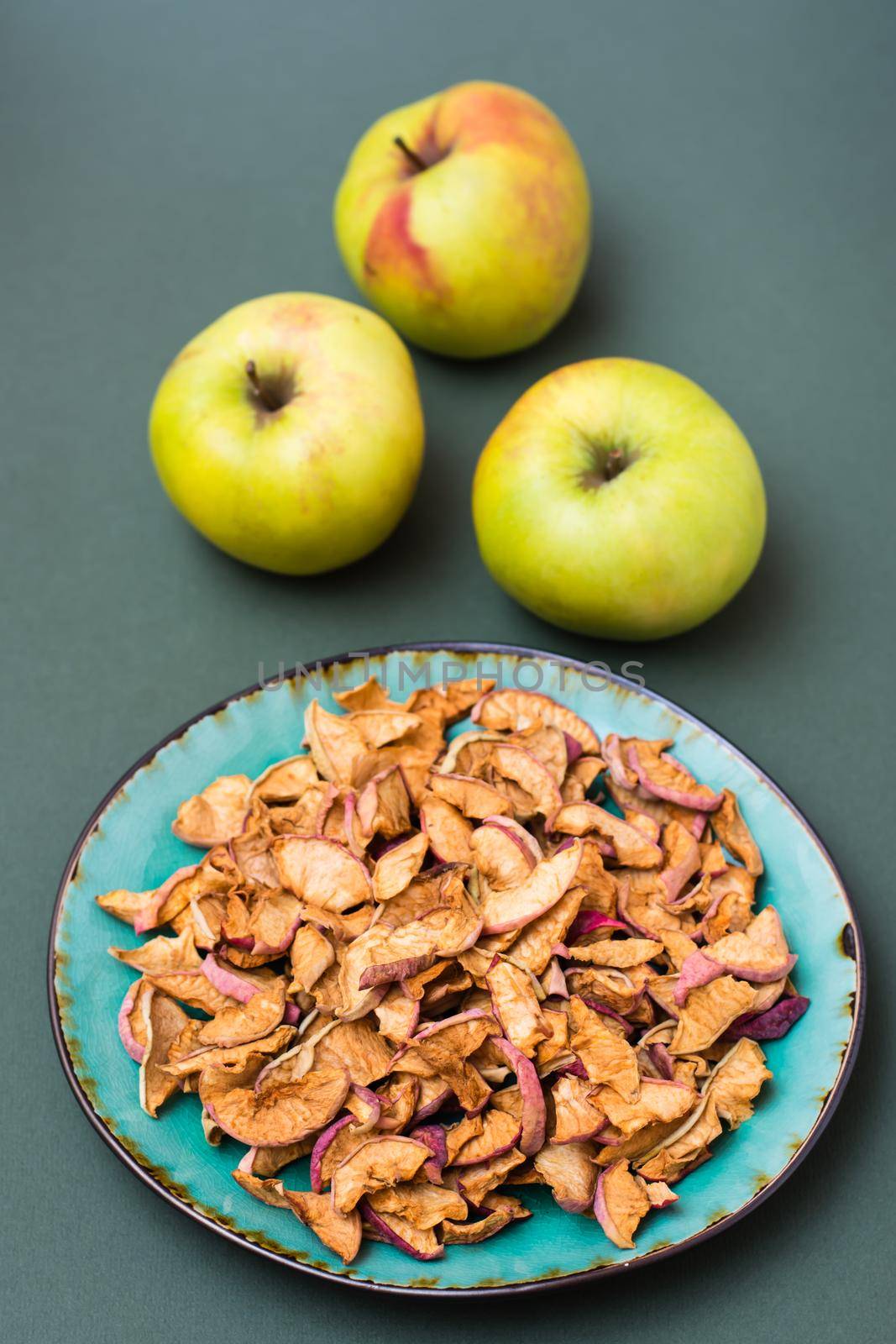 Slices of dry apples on a plate and fresh apples on a green background. Healthy eating. Vertical view by Aleruana