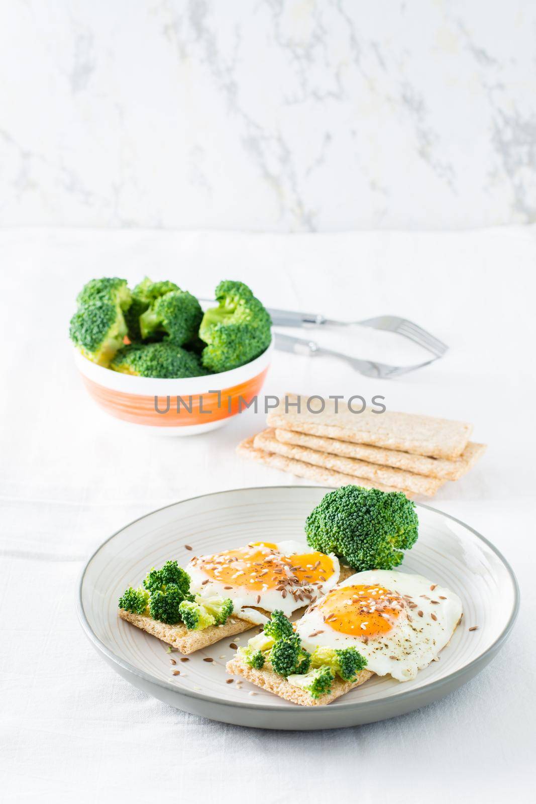 Bruschetta with scrambled eggs and broccoli on a grain crispbread with sesame seeds and flaxseed on a plate and a bowl of broccoli on the table. Vertical view