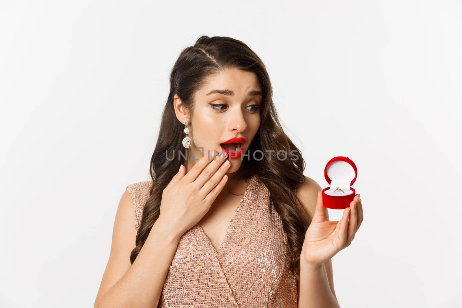 Surprised beautiful woman looking at engagement ring, feeling touched, receive marriage proposal, standing over white background.