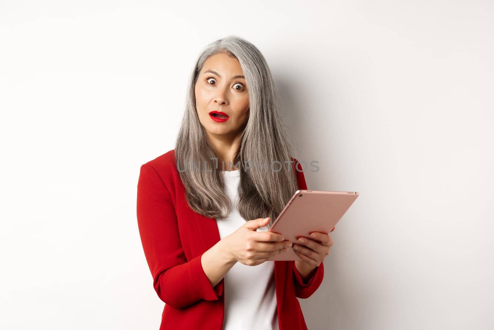 Business. Surprised asian businesswoman looking impressed after reading something on digital tablet, standing over white background.