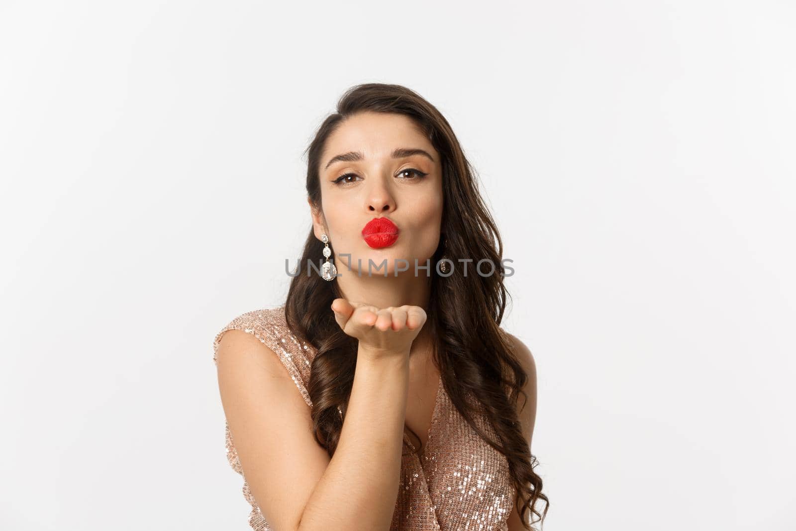 Concept of New Year celebration and winter holidays. Close-up of sensual young woman in dress, pucker lips and blowing air kiss at camera, white background by Benzoix