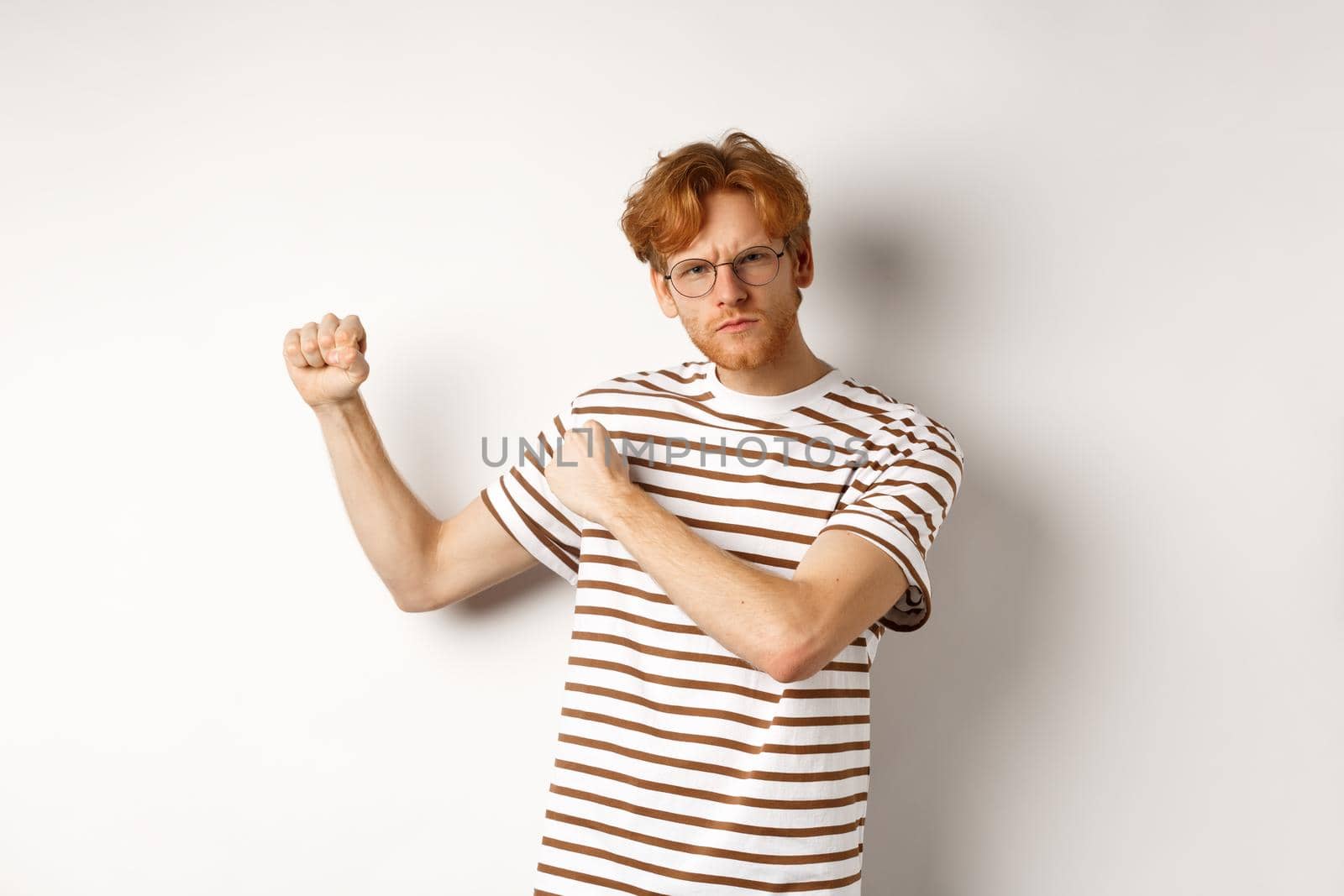 Serious and confident redhead man in glasses raising fists, ready for fight, staring angry at camera while shadow boxing, standing over white background by Benzoix