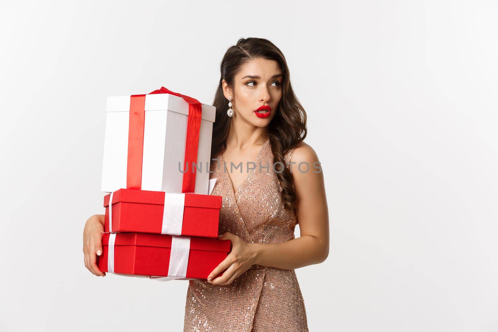 New Year, Christmas and celebration concept. Attractive young woman in elegant dress, looking away, carry gifts, standing over white background by Benzoix