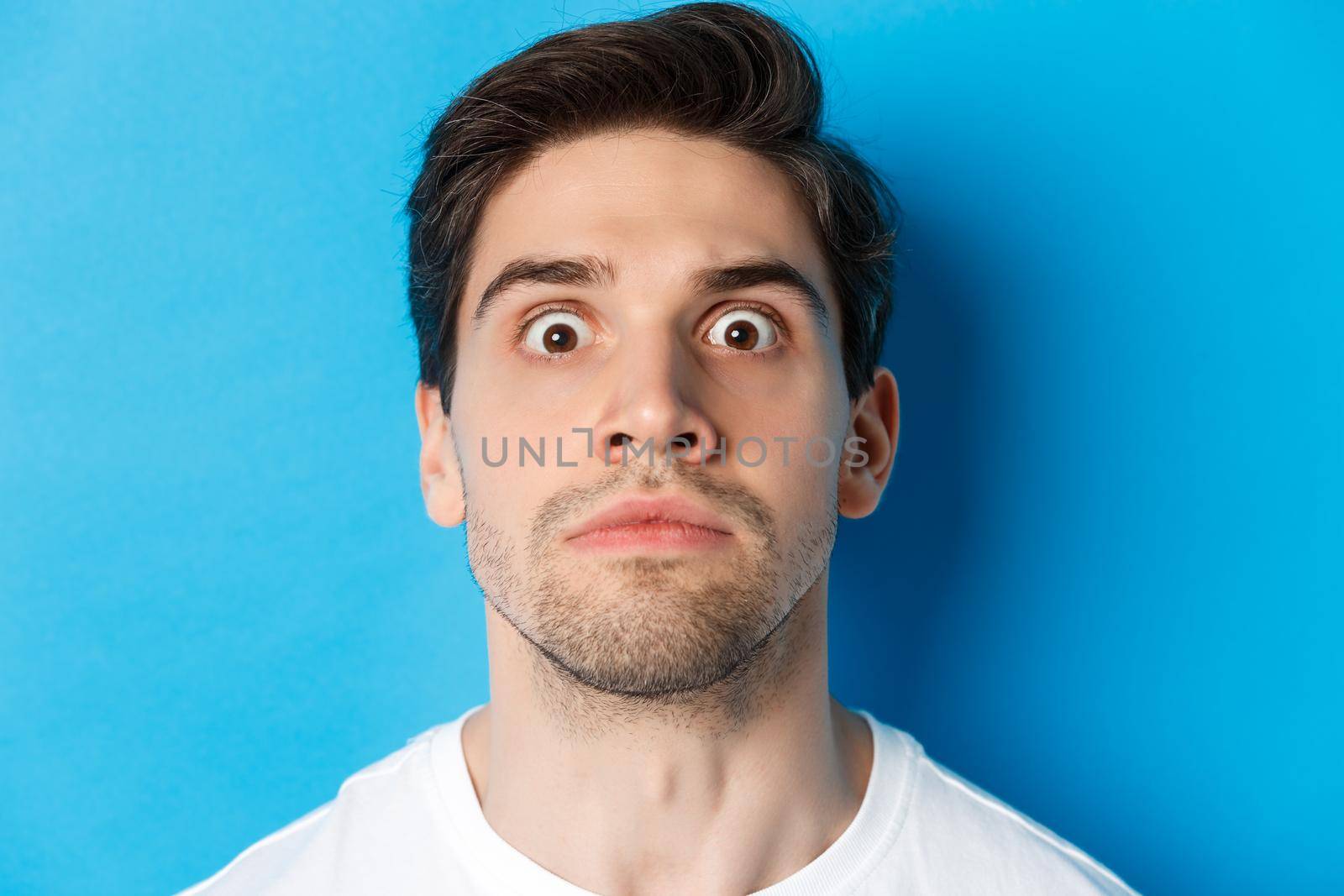 Headshot of pissed-off man losing his temper, looking tensed and angry, standing over blue background by Benzoix