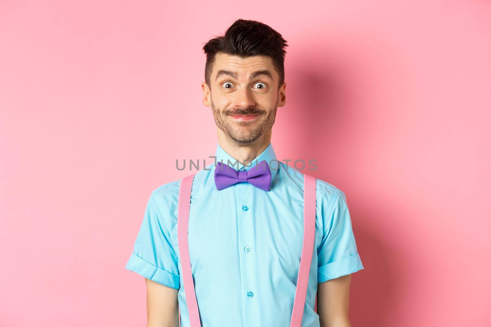 Smiling caucasian man looking excited, standing in classy bow-tie and shirt for romantic date, pink background by Benzoix