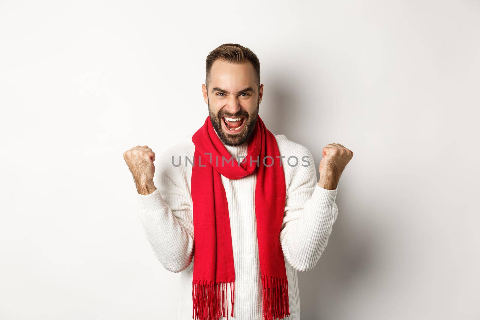 Christmas holidays and New Year concept. Happy man celebrating victory, winning and making fist pumps, achieve goal, saying yes while standing over white background by Benzoix