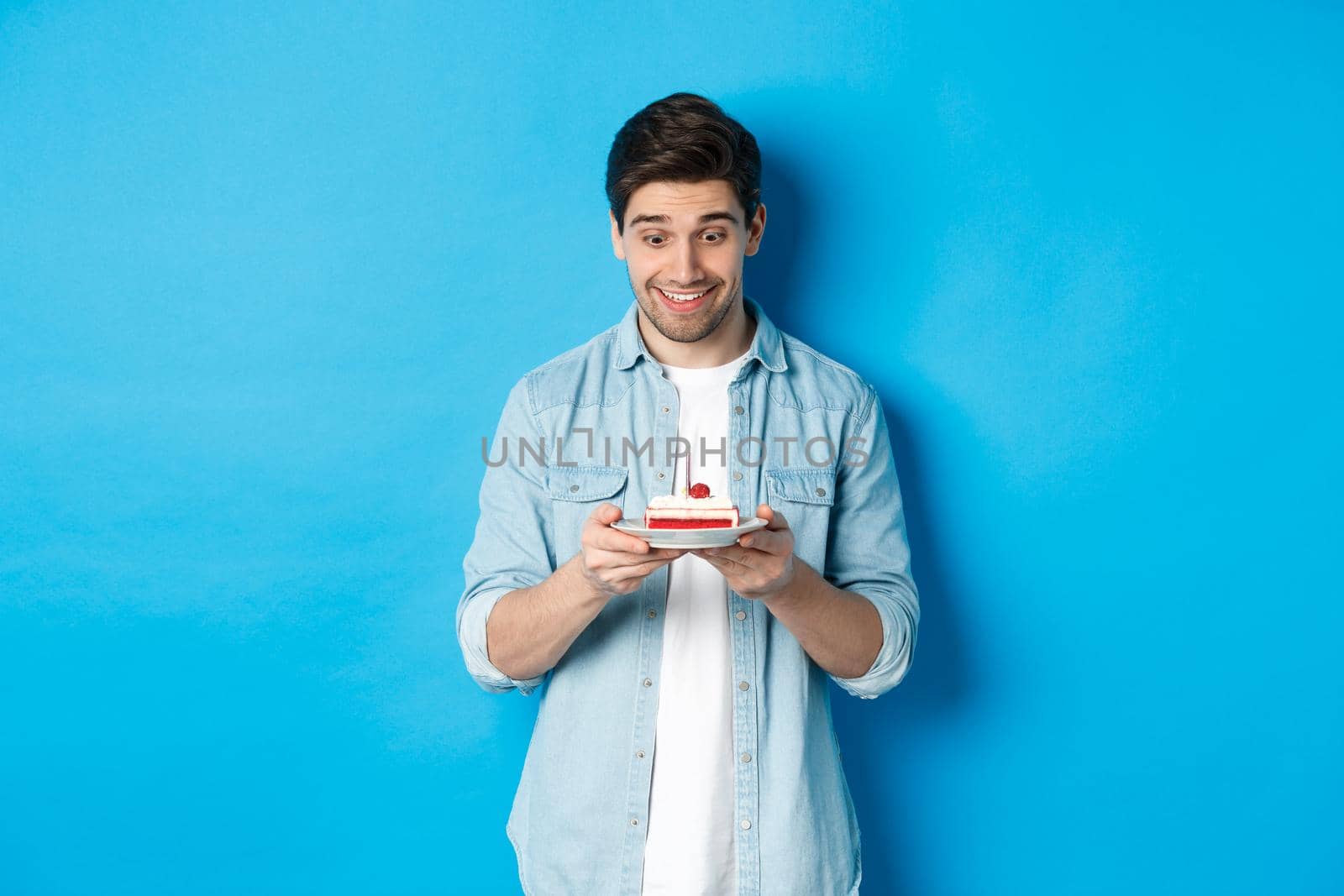 Happy man looking at birthday cake and making with, standing over blue background by Benzoix
